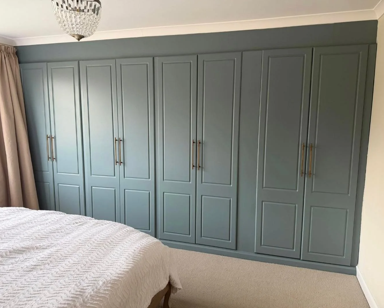Bedroom with large built-in closet painted gray, a bed with white textured bedding, beige curtains, and a ceiling light fixture.