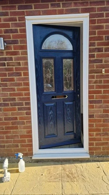 Blue front door with decorative glass panels, surrounded by a white door frame, set in a red brick exterior wall.