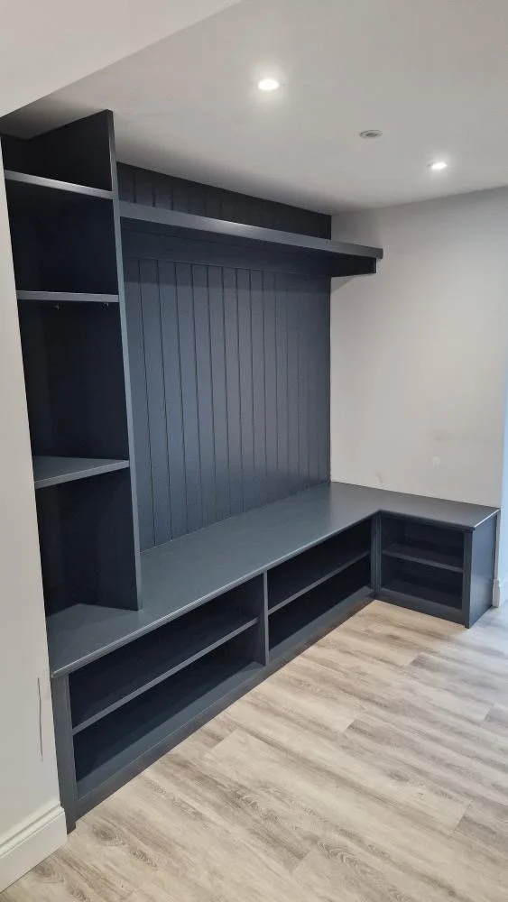 Dark gray built-in shelving and seating unit against a wall in a room with light-colored wood floor and white ceiling with recessed lighting.