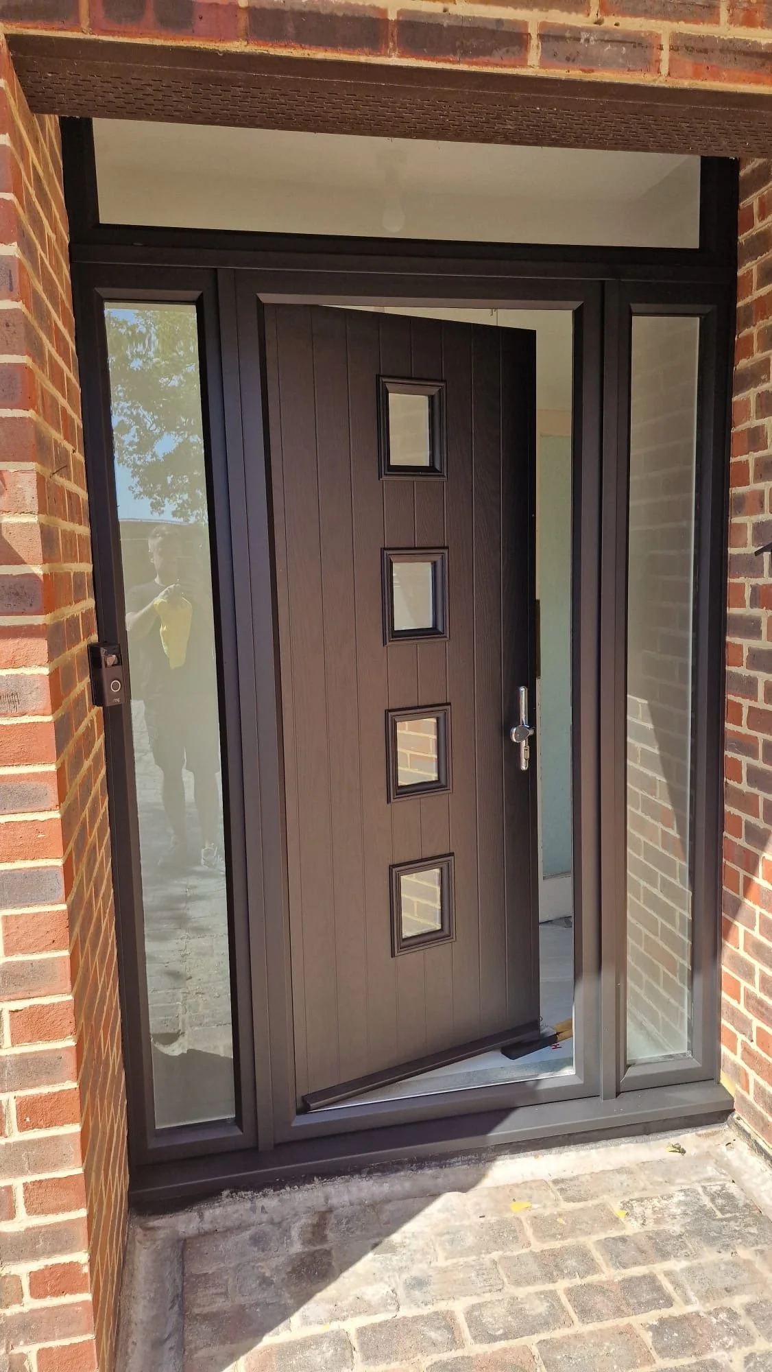 Modern front door with four small square windows, surrounded by glass panels, set in a brick wall.