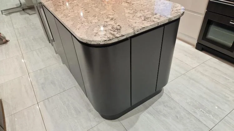 Kitchen island with a granite countertop and dark gray cabinets, located on a tiled floor.