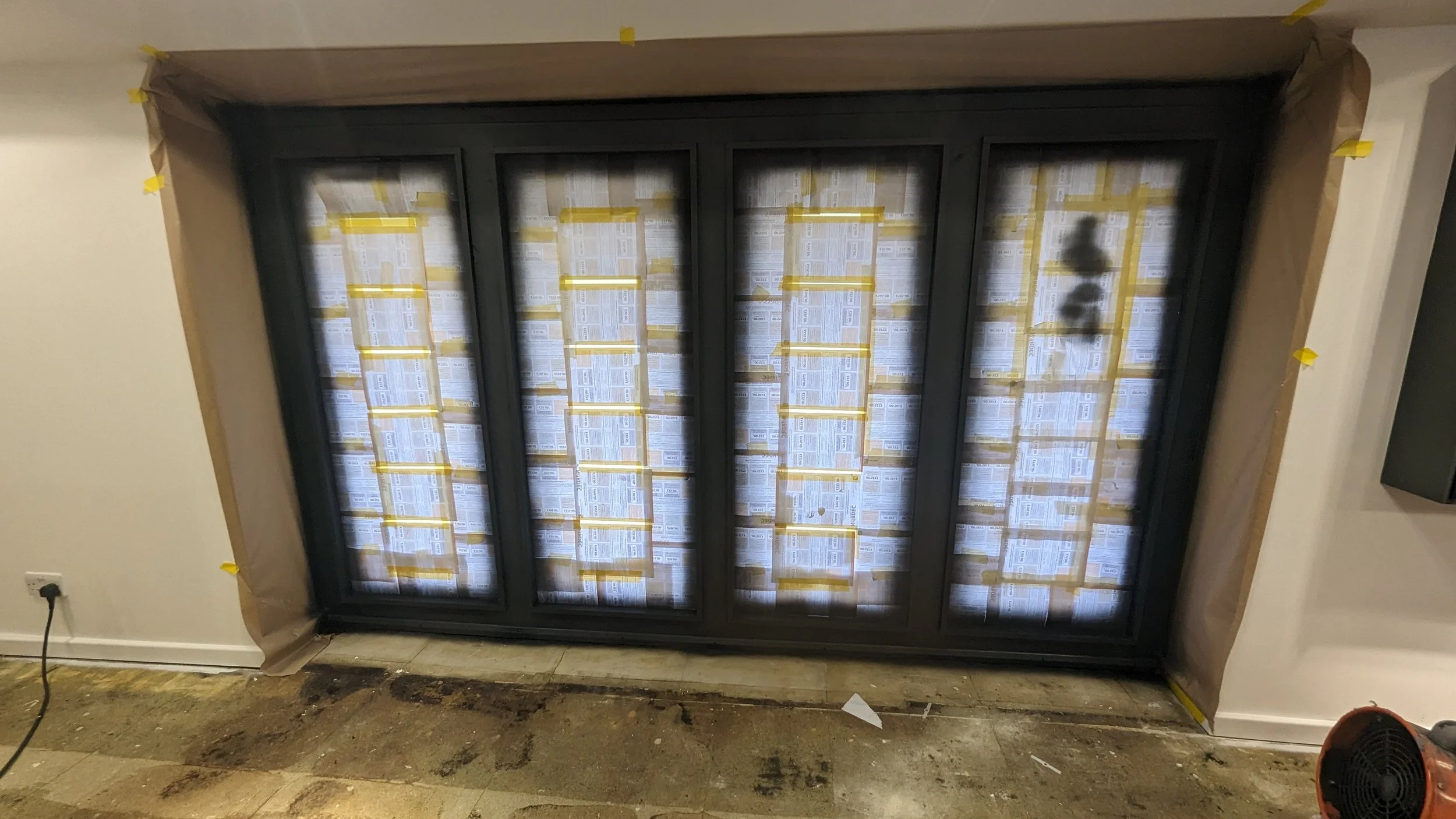 L-shaped black window frame installed in a wall, covered with protective paper and tape during construction or renovation.