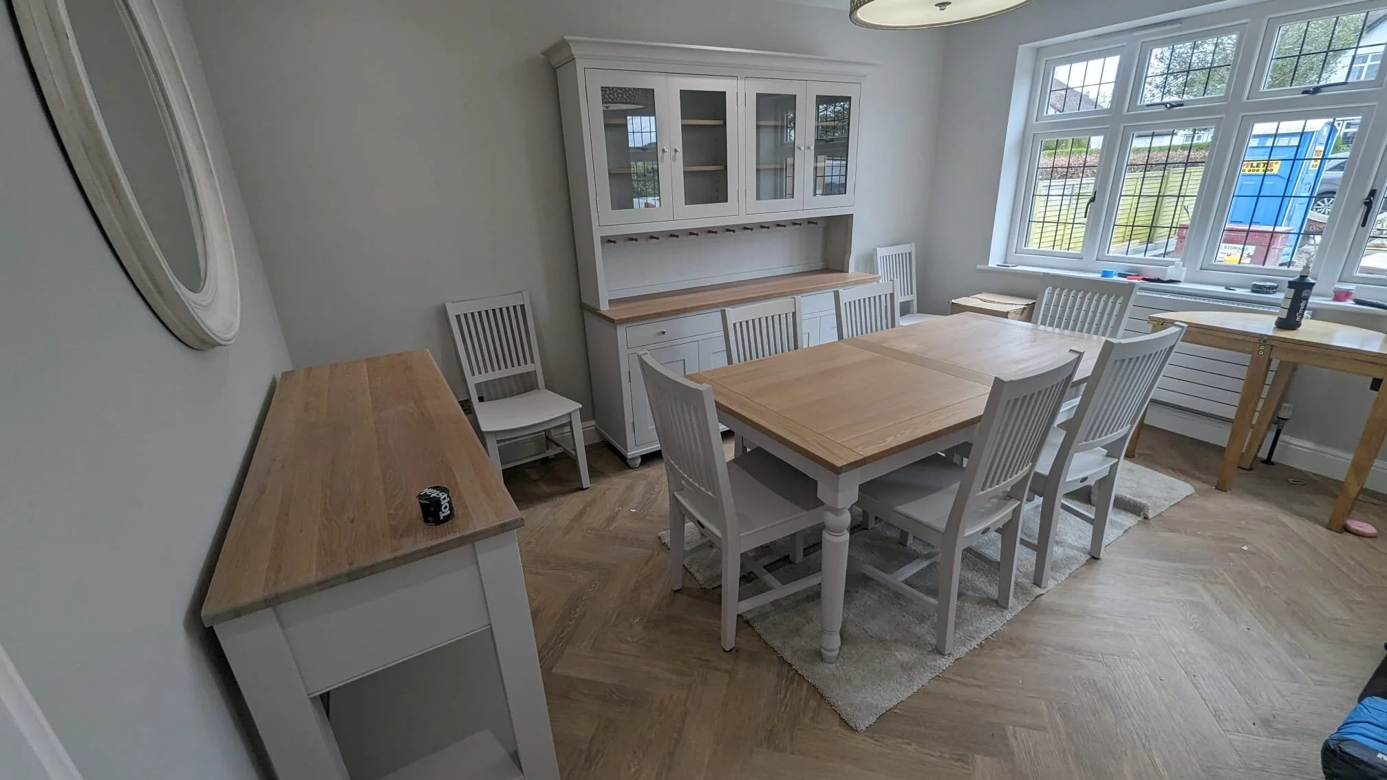 Dining room with a wooden dining table and six matching chairs, white built-in cabinet, large window with natural light, and wooden flooring.