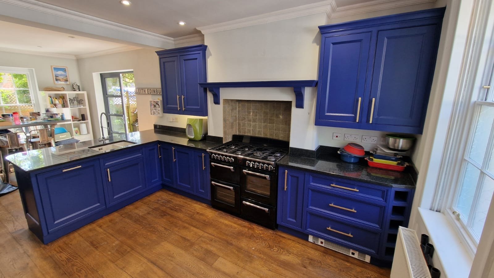 Kitchen with blue cabinets, black countertop, stove, green kettle, and window with natural light.