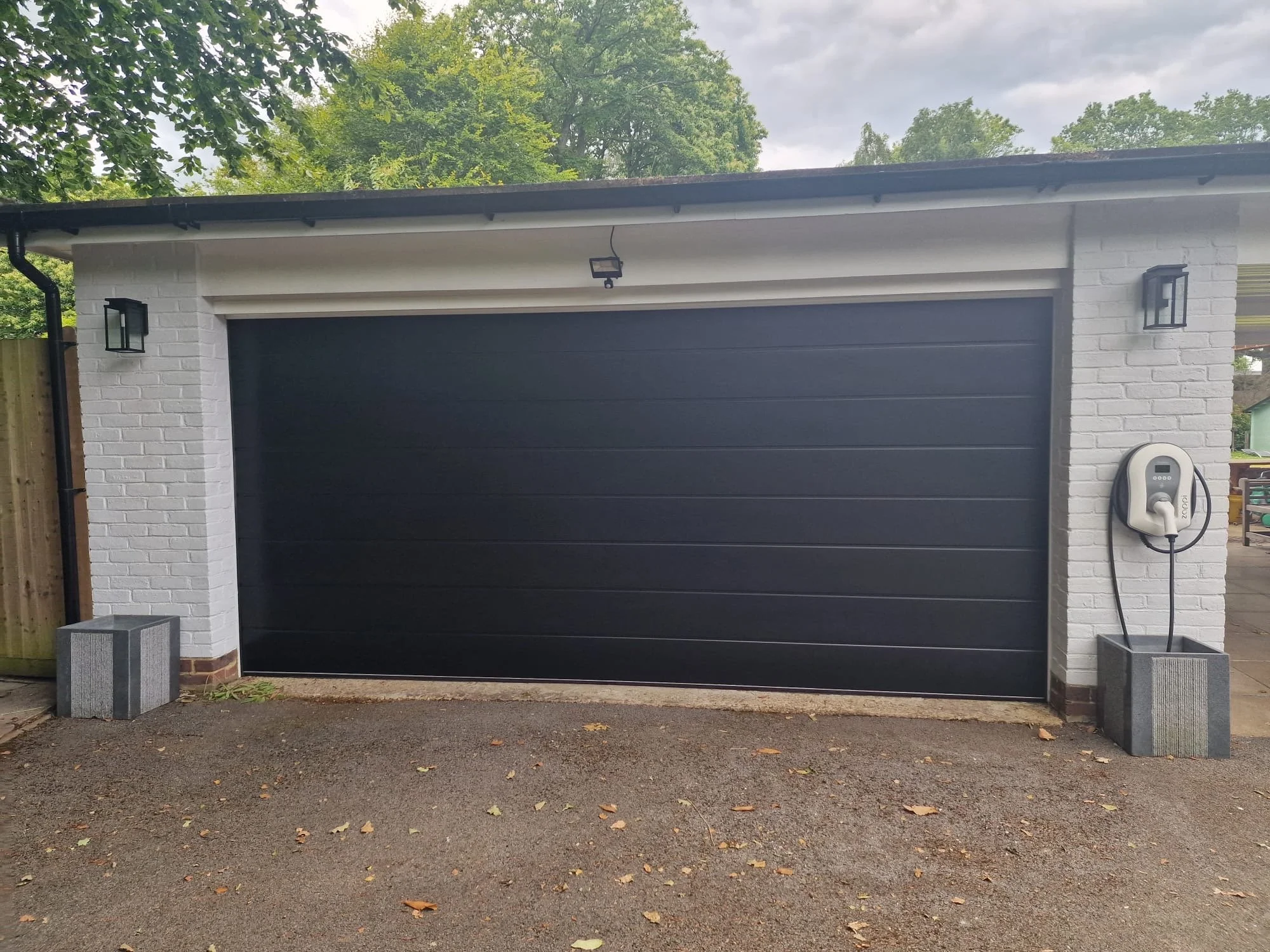 Front view of a two-story brick house with a two-car garage, a small porch, and a lawn with two trees on either side.