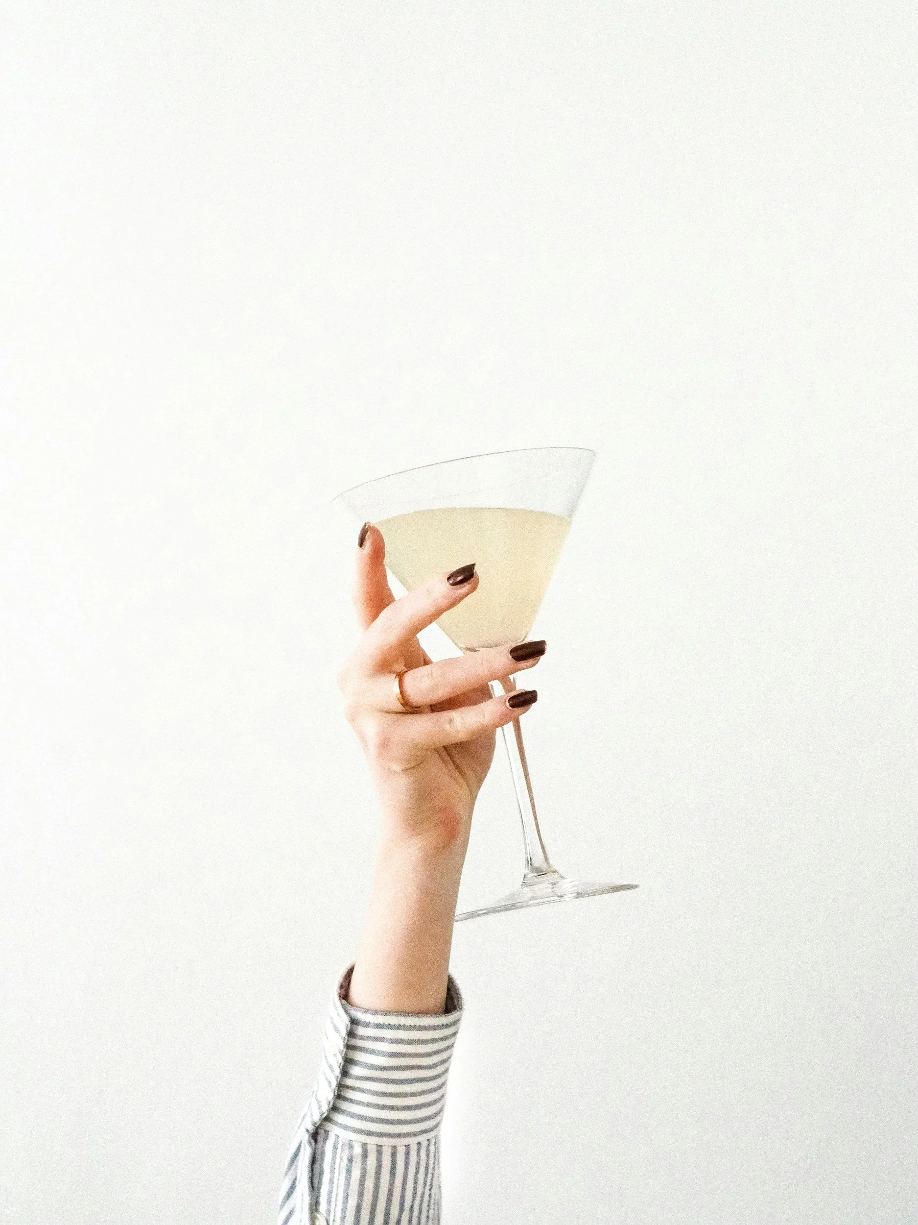 Person holding a martini glass with an off-white beverage against a plain white background.