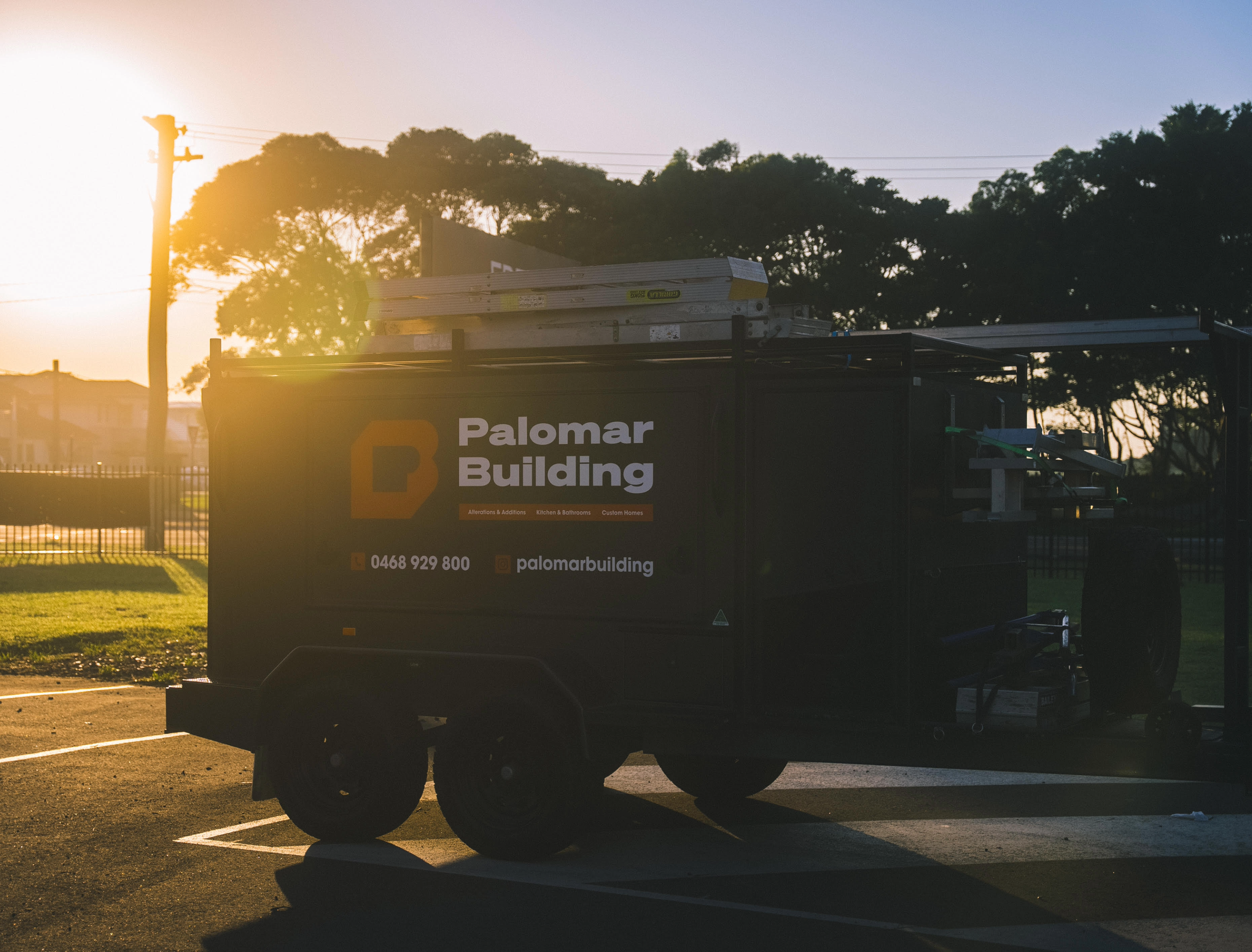 Construction trailer for Palomar Building parked in an outdoor lot during sunset with trees and utility poles in the background.