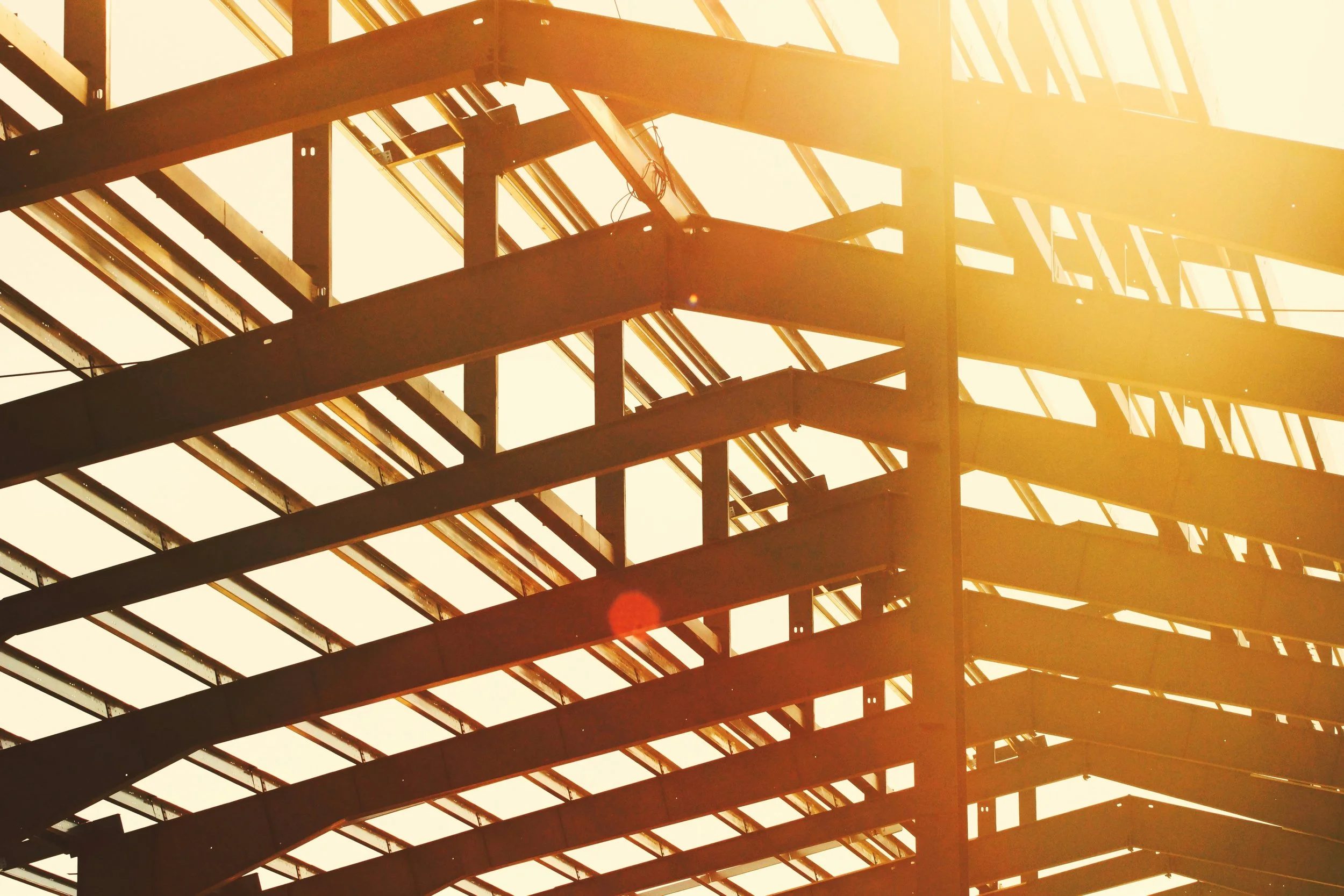 Sunlight illuminating the framework of a building under construction with steel beams and glass panels.