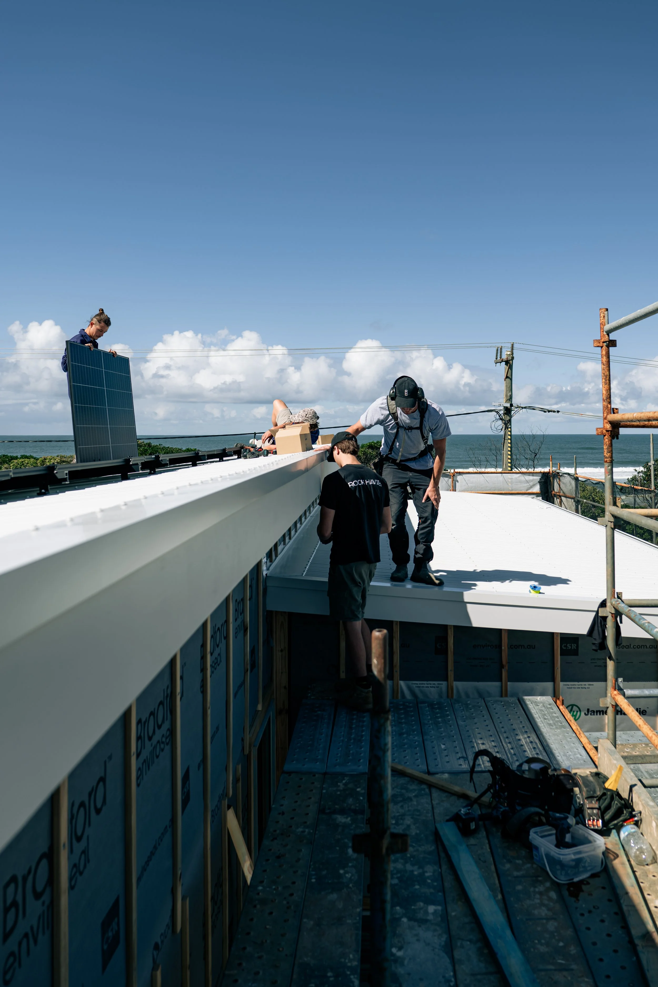 A group of construction workers installing a roof on a building near the coast on a sunny day.