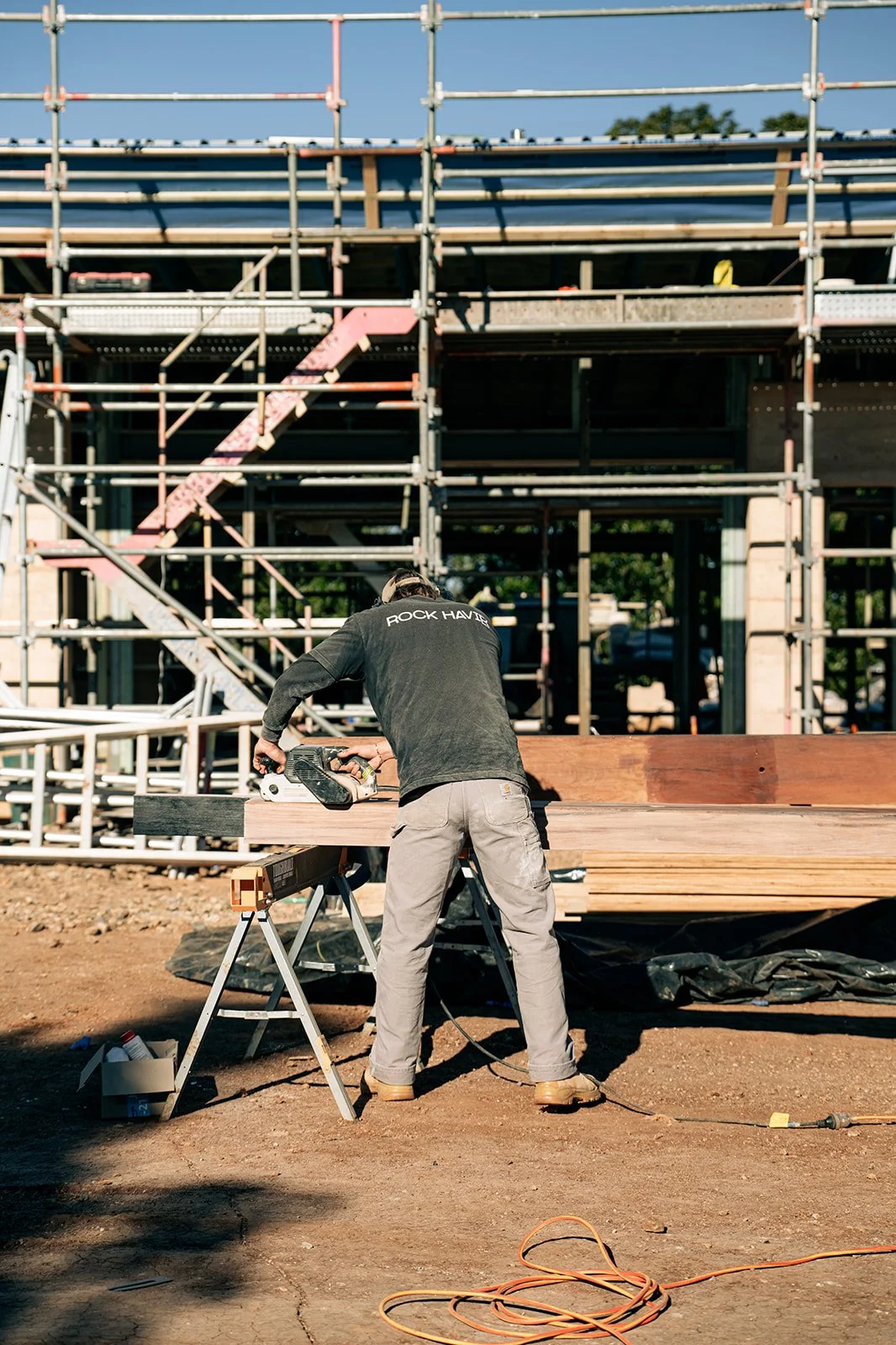 A construction worker cutting wood at a building site with scaffolding and a building framework in the background.