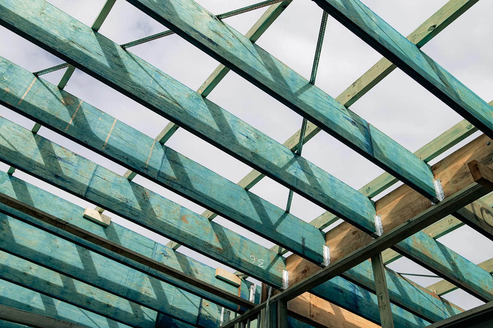 Wooden framing for a building under construction, showing beams and supports against a cloudy sky.