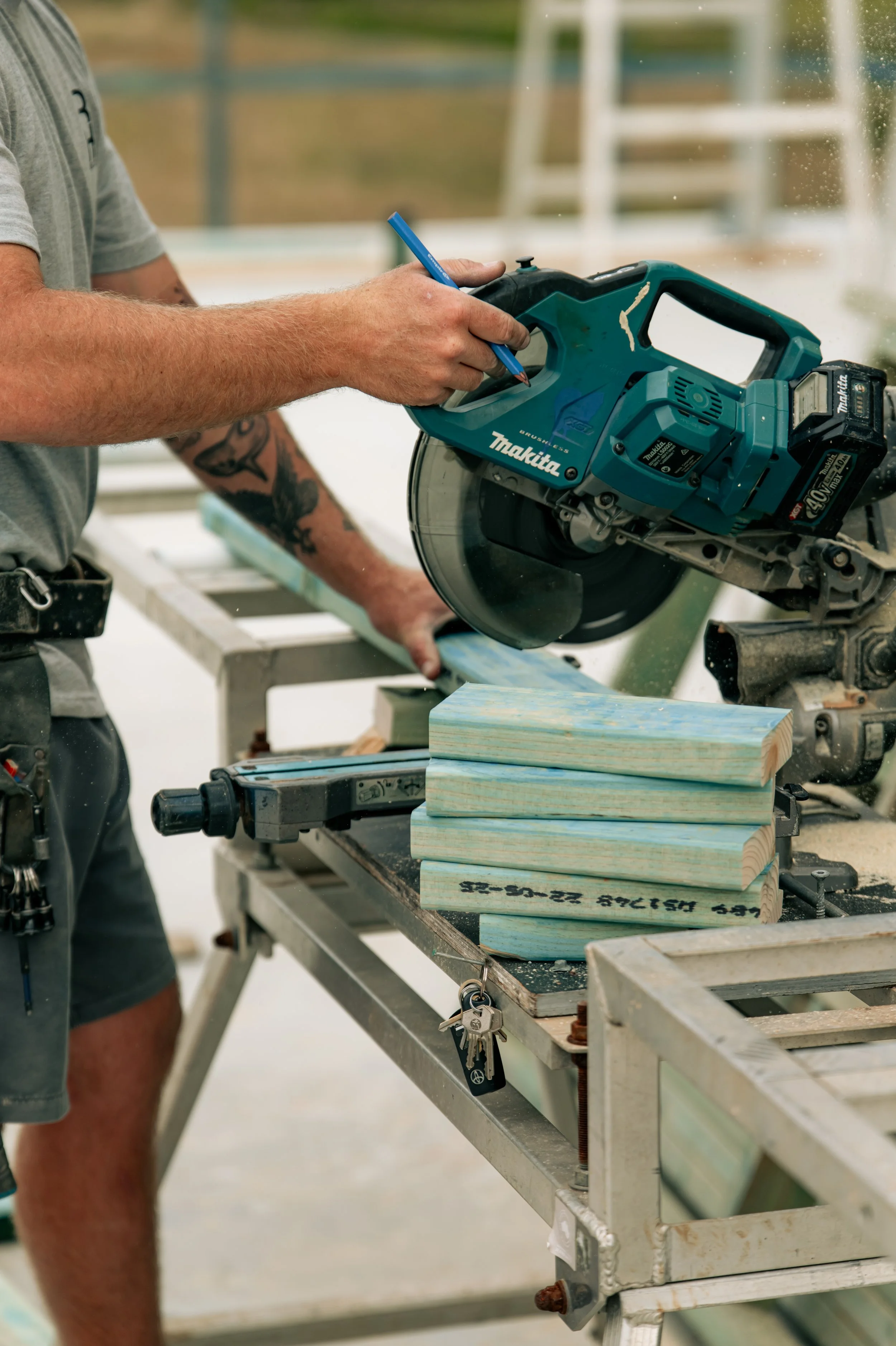 Person using a Makita cordless circular saw to cut a piece of light-colored wood outdoors.