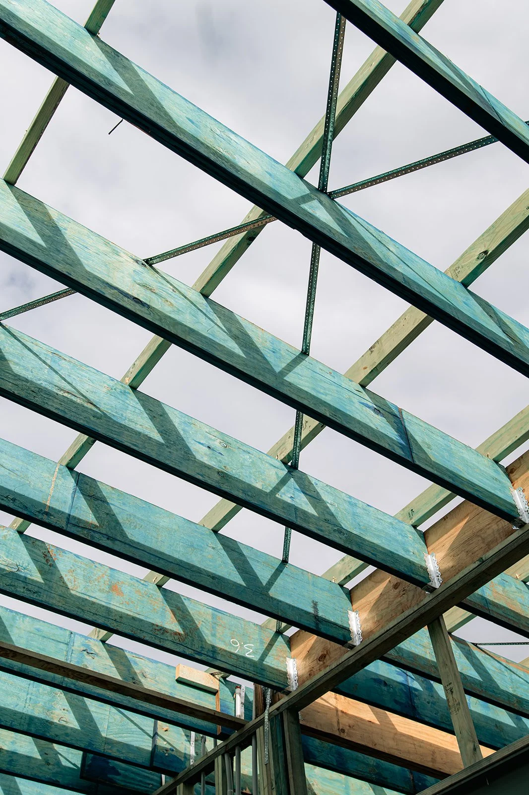 View of a building under construction with wooden beams and framing, casting shadows on each other against a cloudy sky.