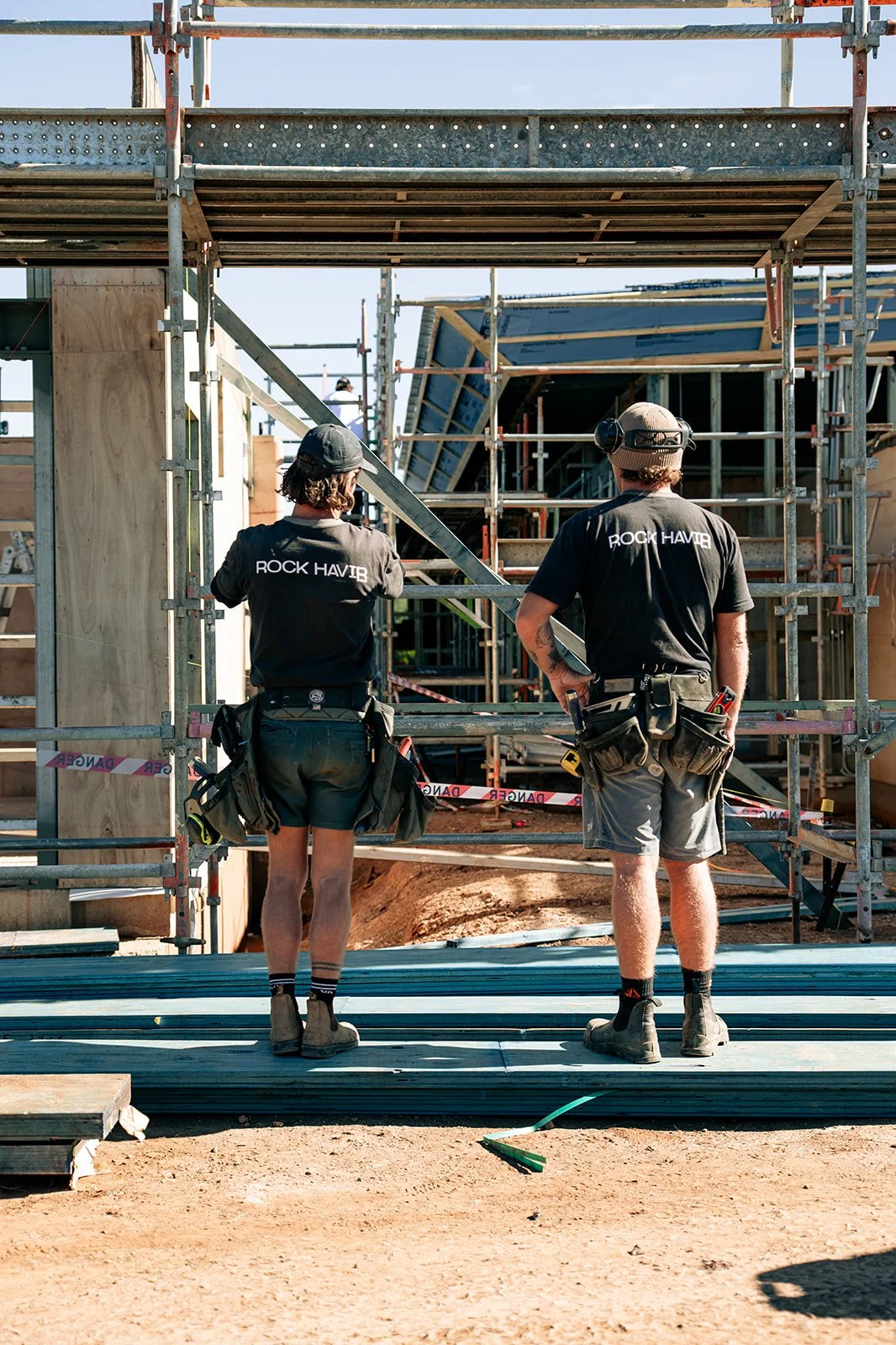 Two construction workers wearing black T-shirts with 'Rock Havir' on the back.