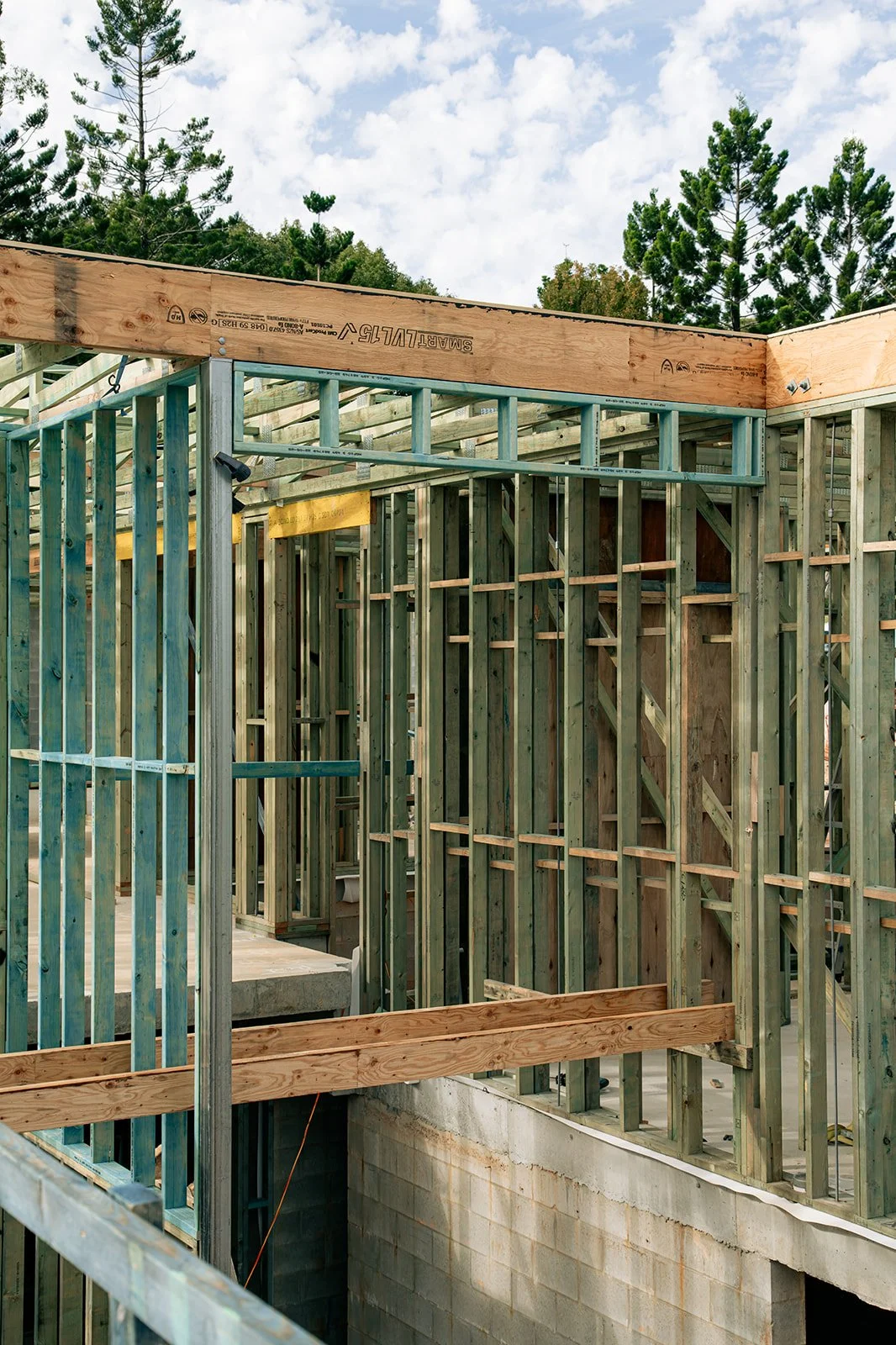 Wood framing and wall supports for a building under construction, with trees and sky visible in the background.