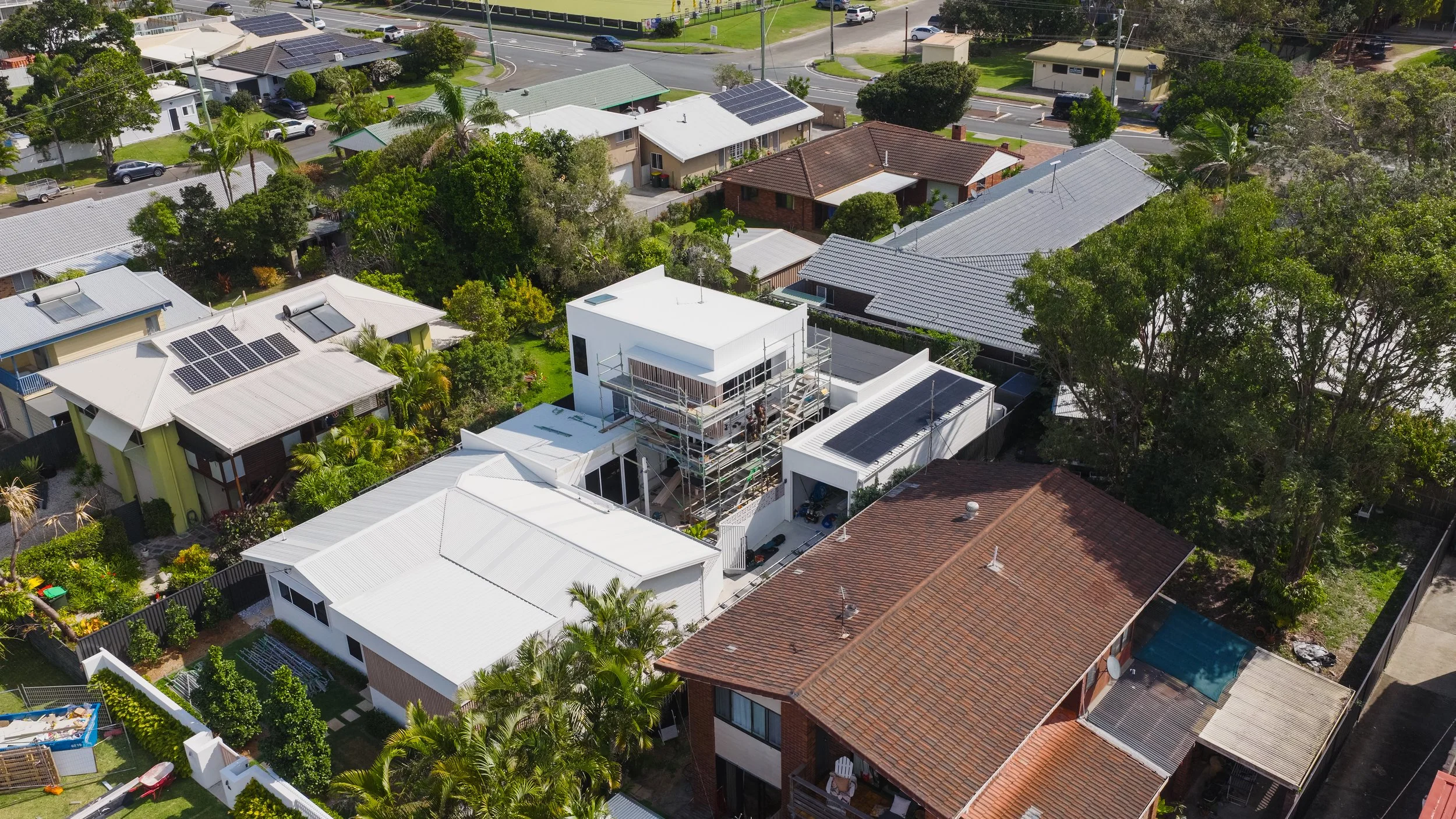 Aerial view of a residential neighborhood with several houses, some under construction, with garden areas and trees.