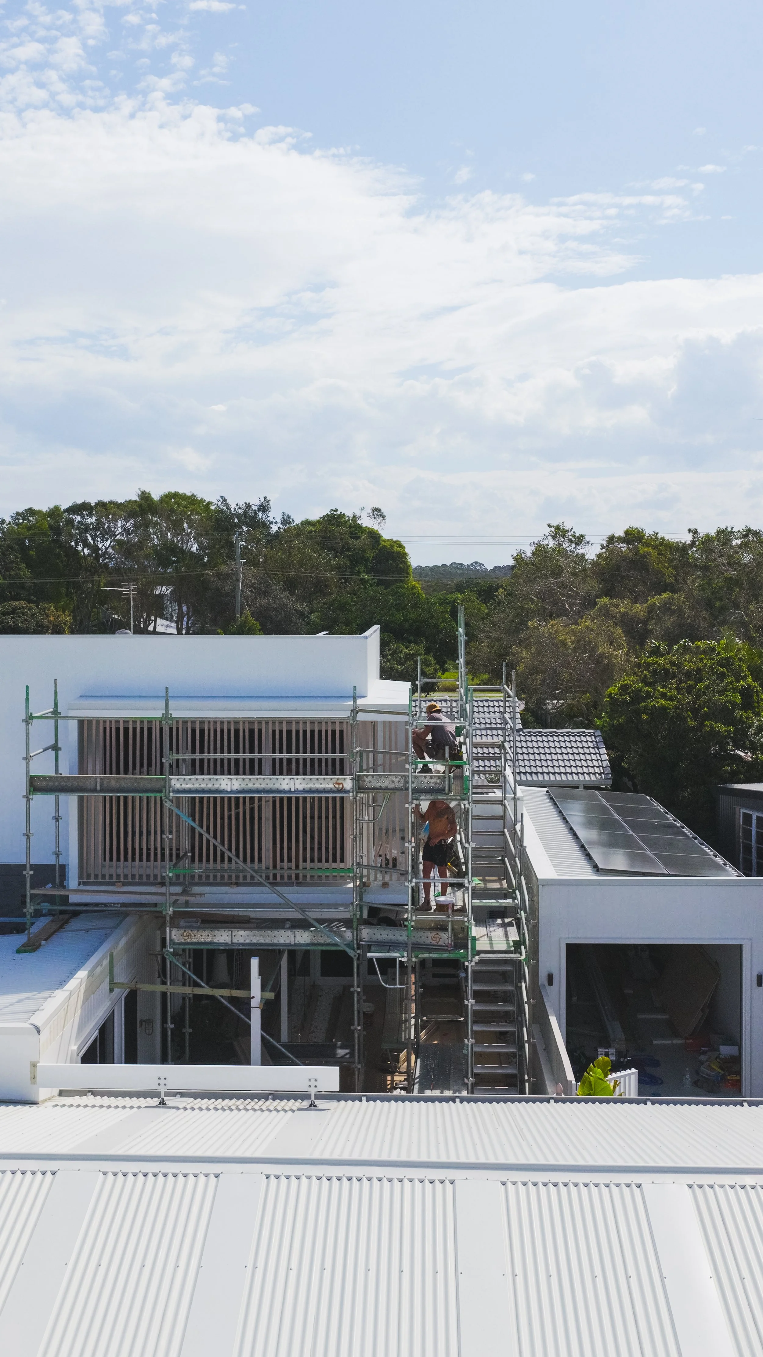 Construction workers on scaffolding repairing or building a roof of a modern white house.