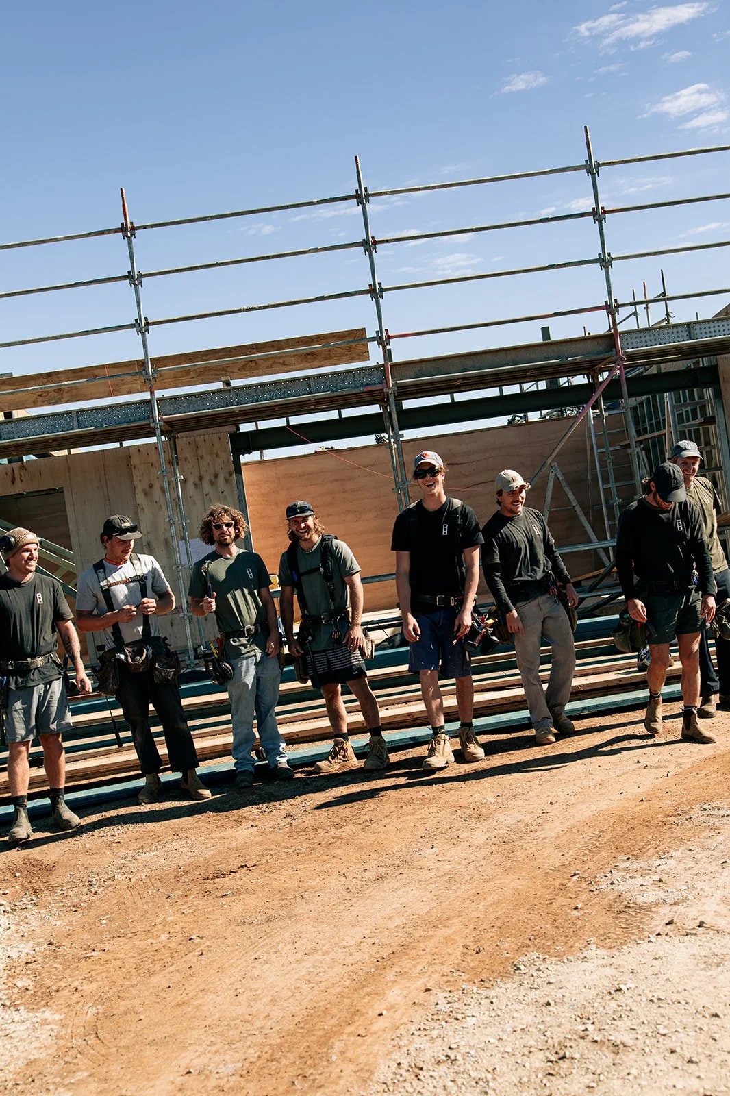 Group of workers on a construction site standing in front of a partially built structure with scaffolding, under a clear blue sky.