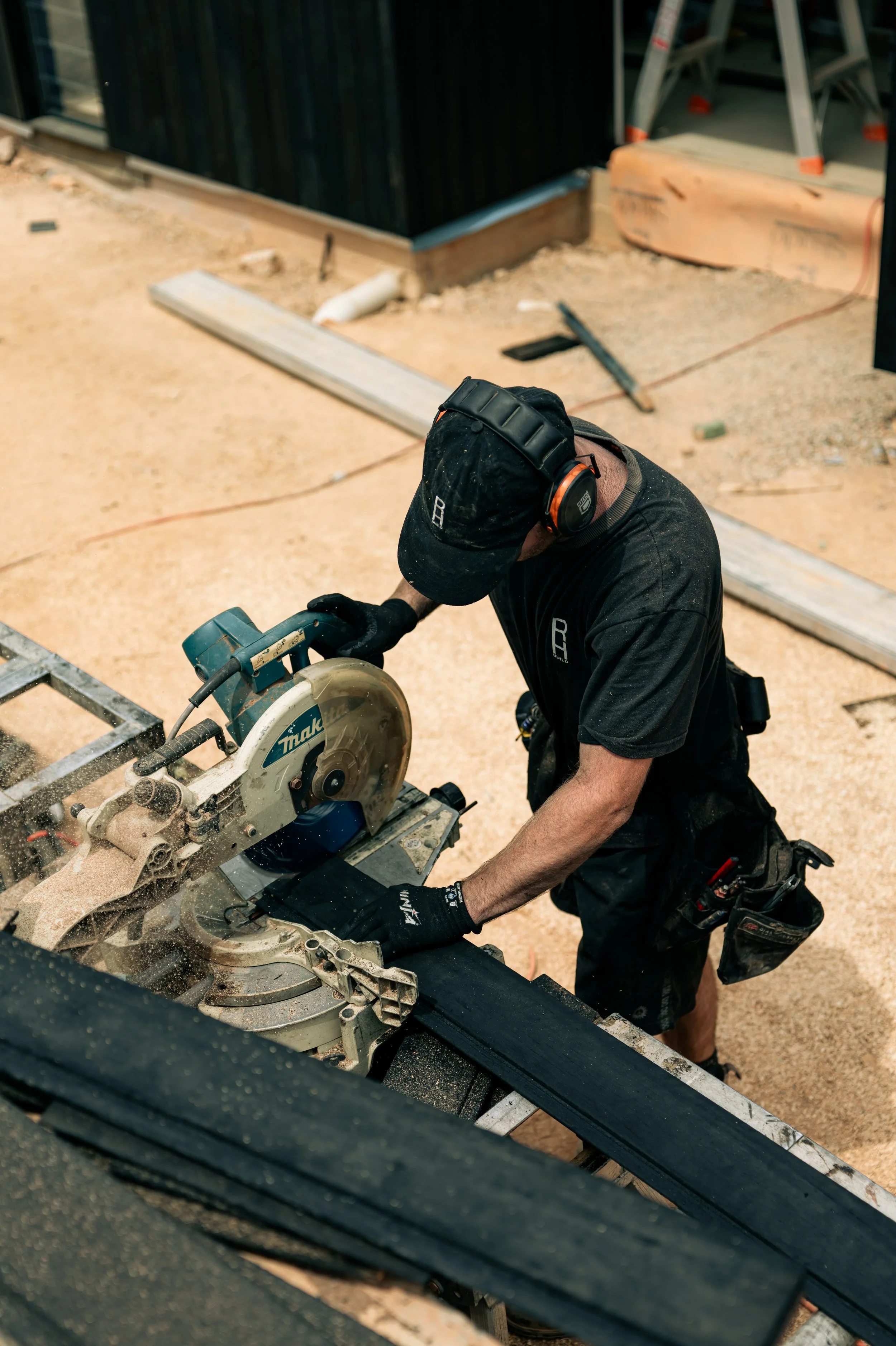 A construction worker using a chop saw to cut a piece of black wood at a construction site.