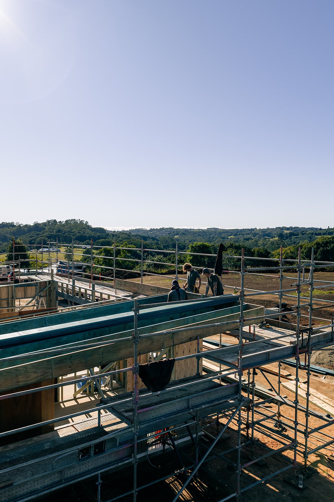 Construction workers building a structure outdoors with scaffolding and wooden frame under a clear sky.