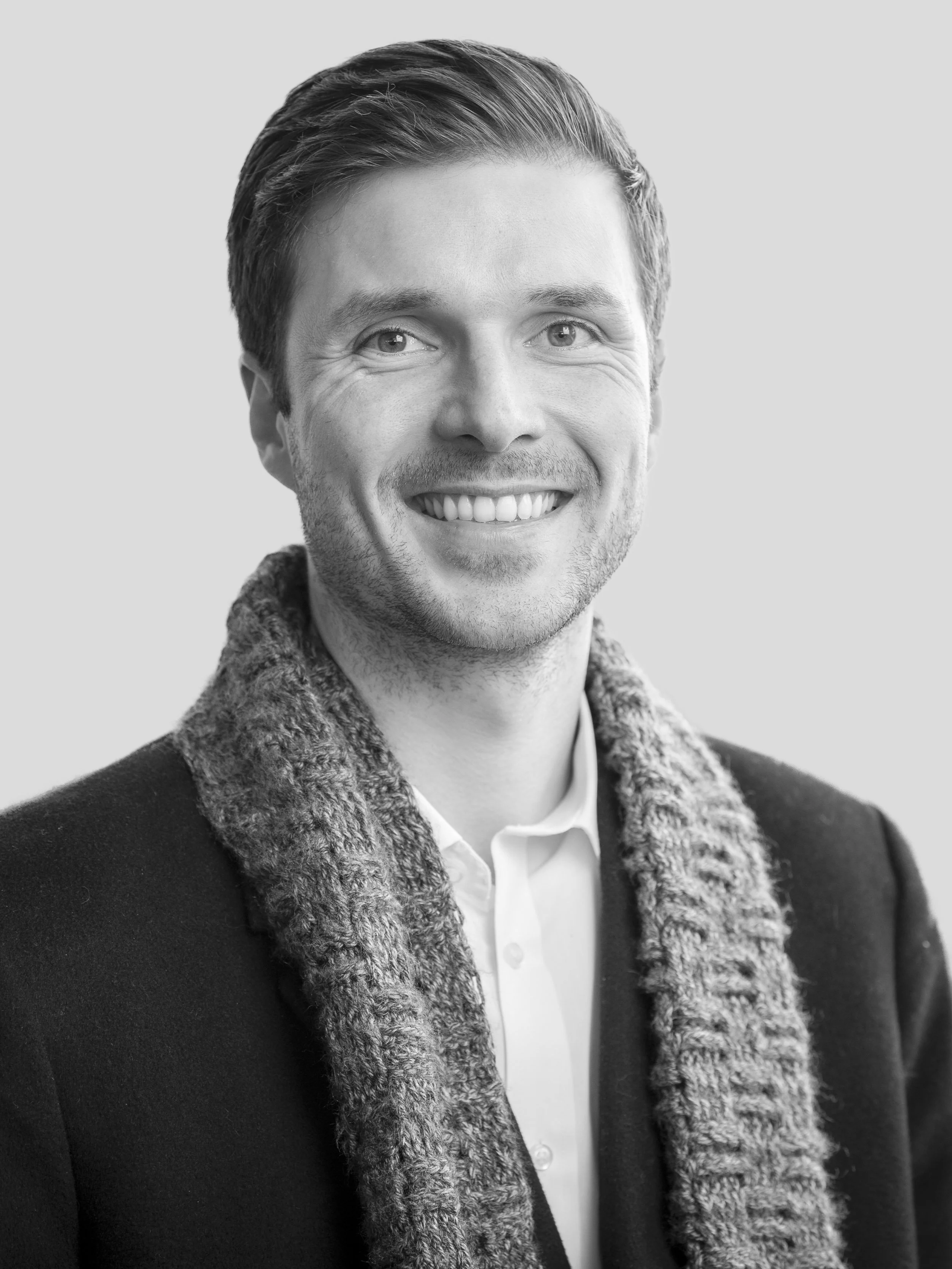 Black and white portrait of a smiling man wearing a wool scarf and a white shirt.