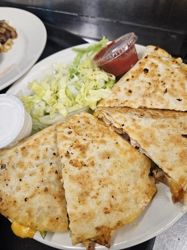 Plate with two quesadillas, shredded lettuce, a cup of salsa, and a small container of sour cream.