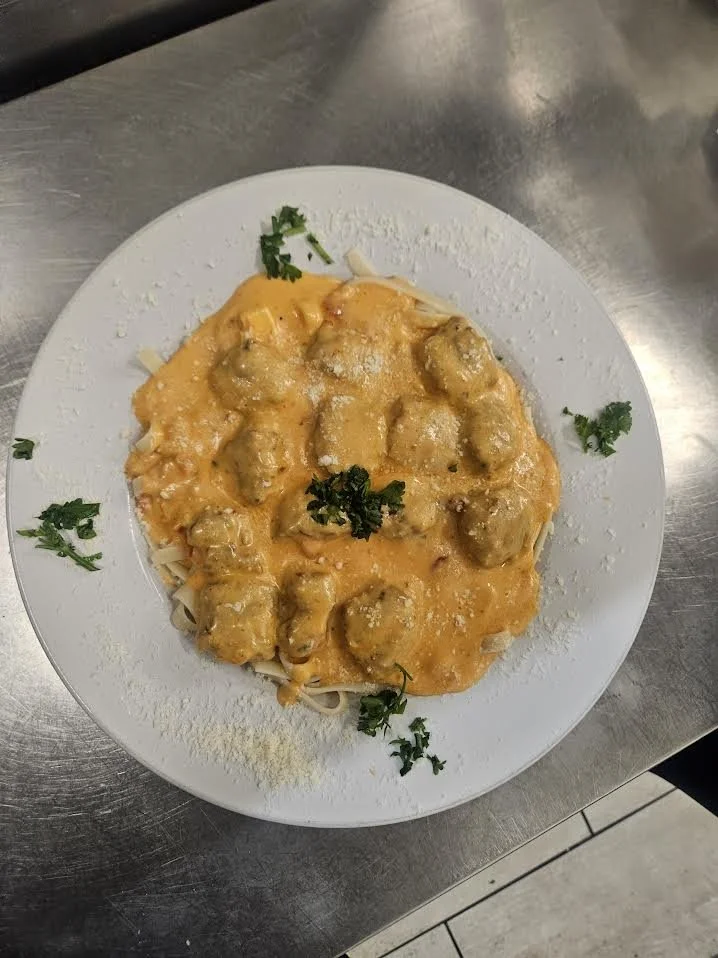 Plate of pasta with meatballs in orange cheese sauce, garnished with parsley.
