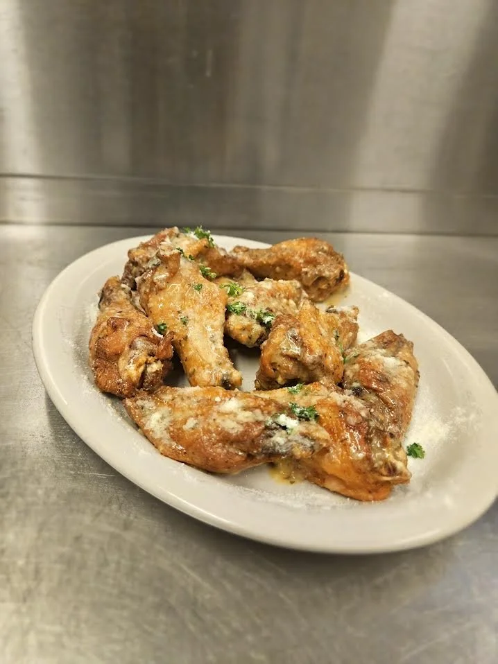 Plate of cooked chicken wings garnished with parsley, placed on a stainless steel surface.