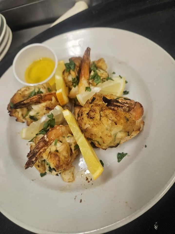 A white plate with grilled shrimp, lemon wedges, parsley, and a small dish of yellow sauce.