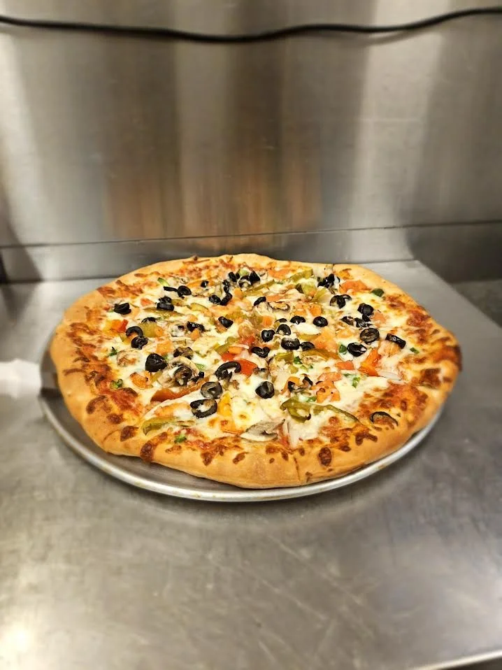 Cheese pizza topped with black olives, green peppers, and mushrooms placed on a metal countertop.