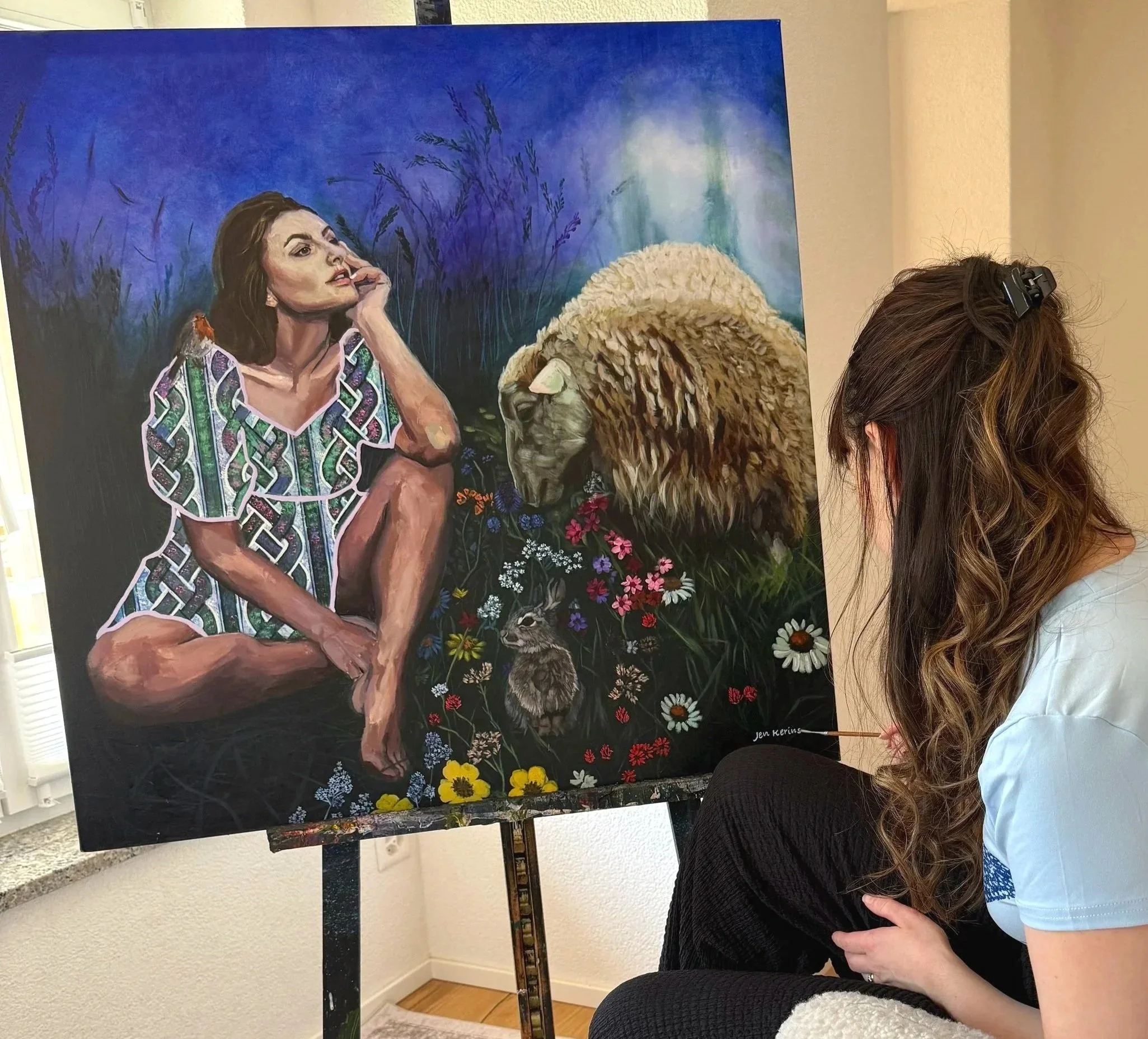 A woman with long dark hair painting a realistic portrait of a woman on a large canvas, with a nature scene and colourful abstract background, in an indoor setting.