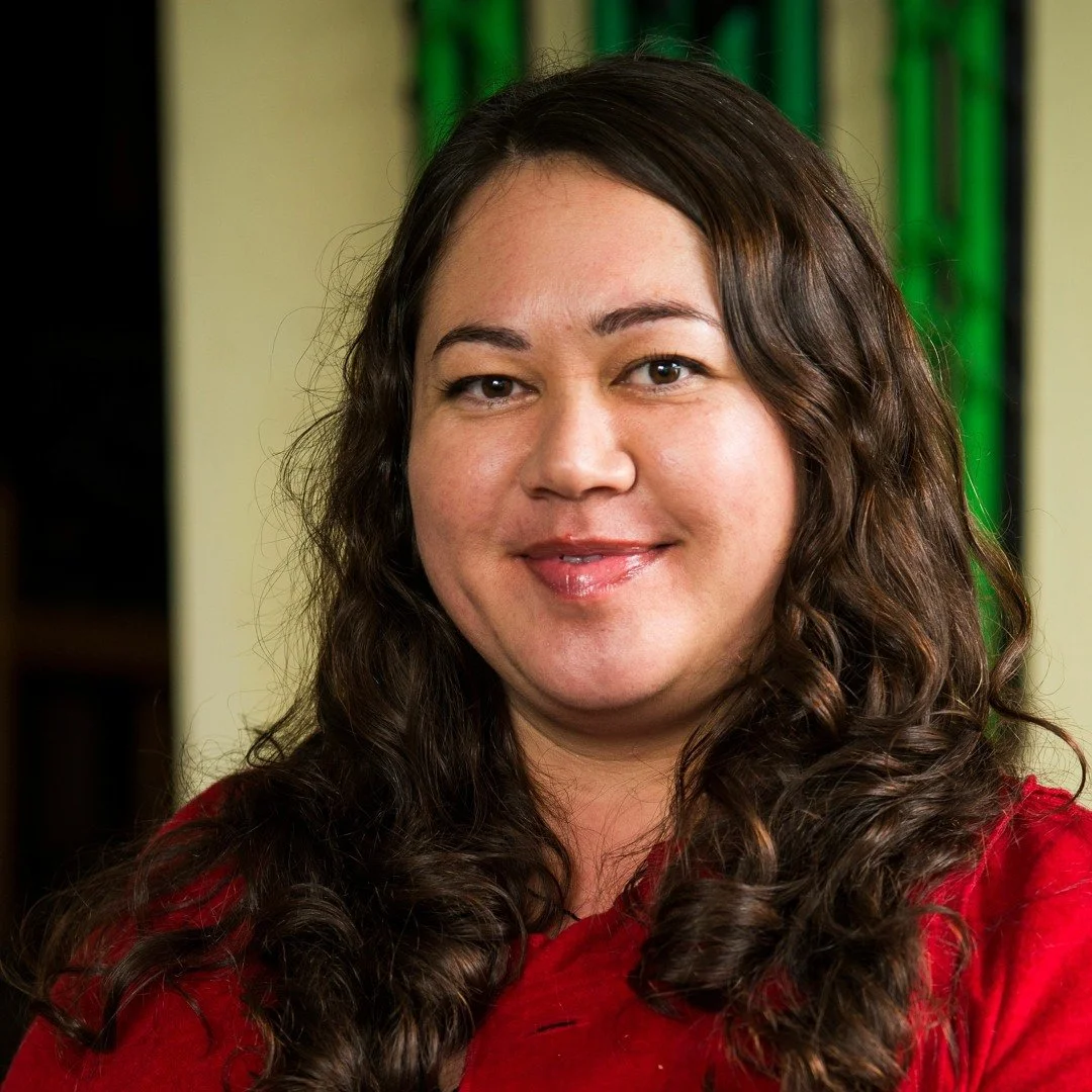 A woman with long curly brown hair, wearing a red top, smiling at the camera.