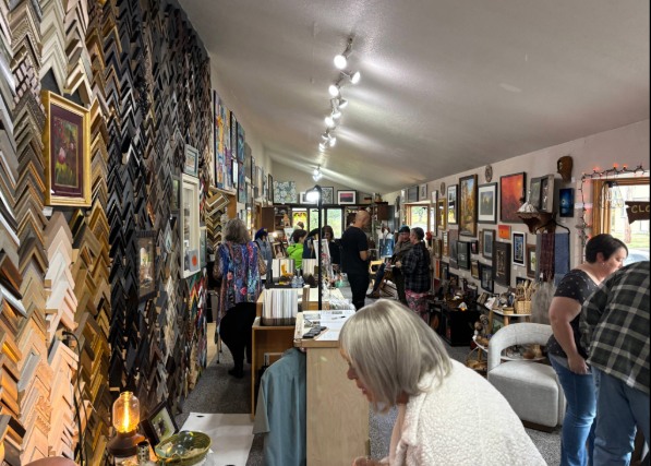 Interior of an art gallery with people browsing and artwork displayed on walls and shelves.