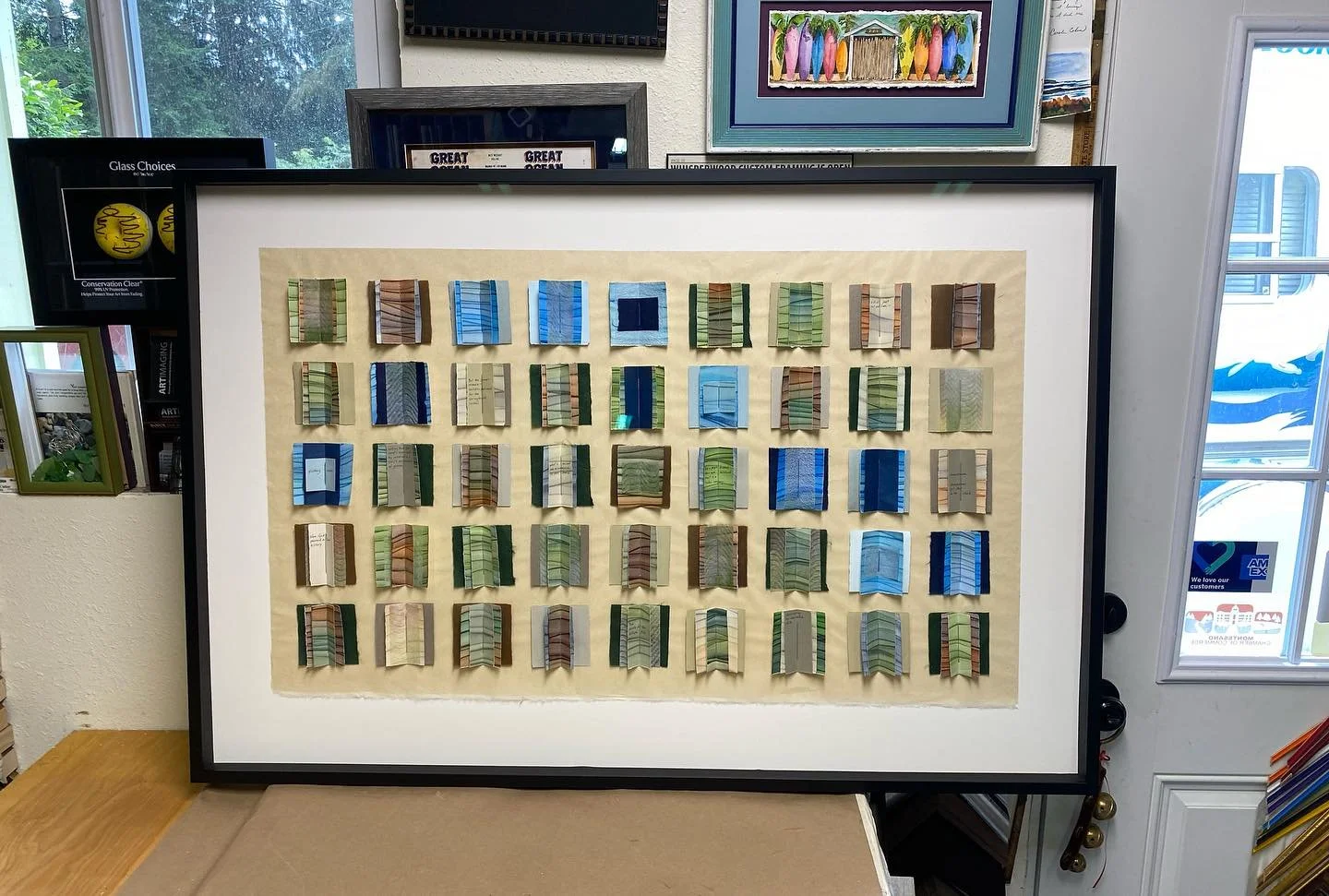 A framed display of fabric swatches arranged in a grid pattern, featuring a variety of colors and patterns.