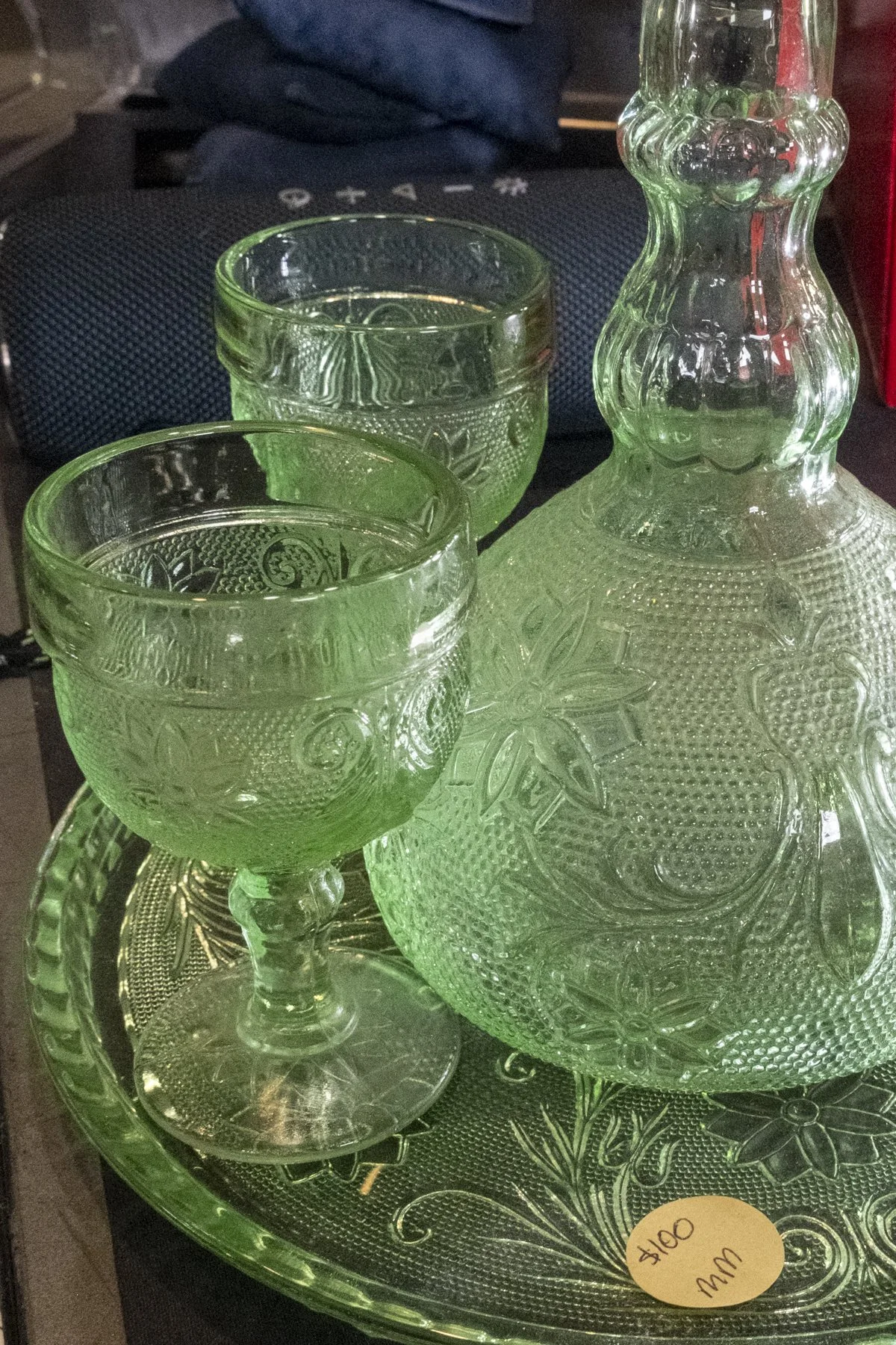 Green glassware set including two goblets and a decanter on a matching green tray with floral patterns, displayed for sale at $10.