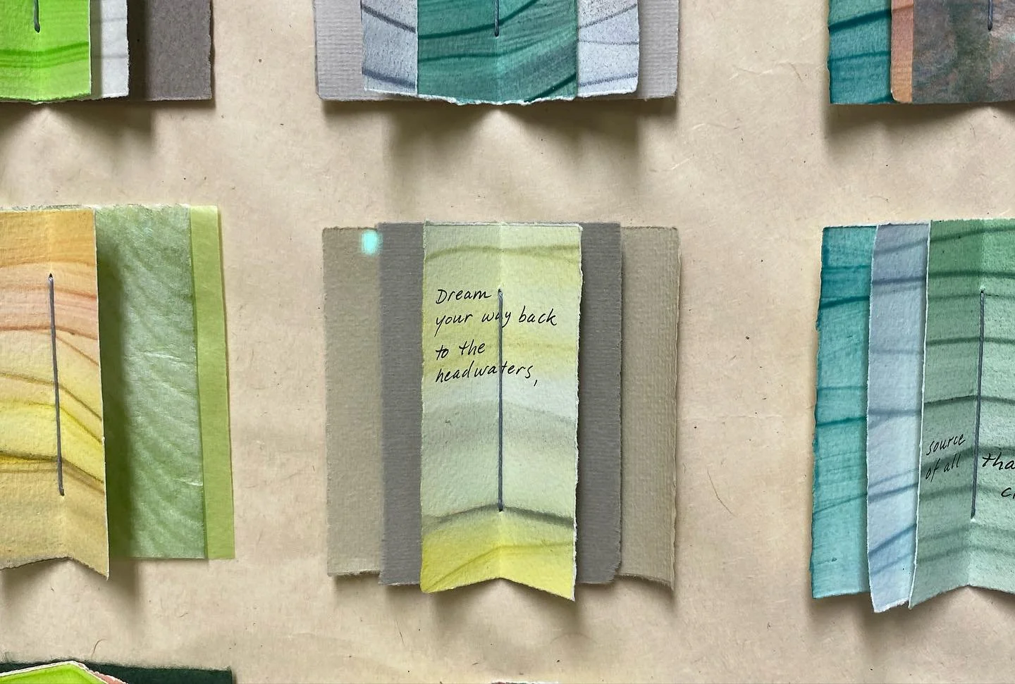 Colorful paper bookmarks with handwritten quotes, arranged in a display on a beige surface.