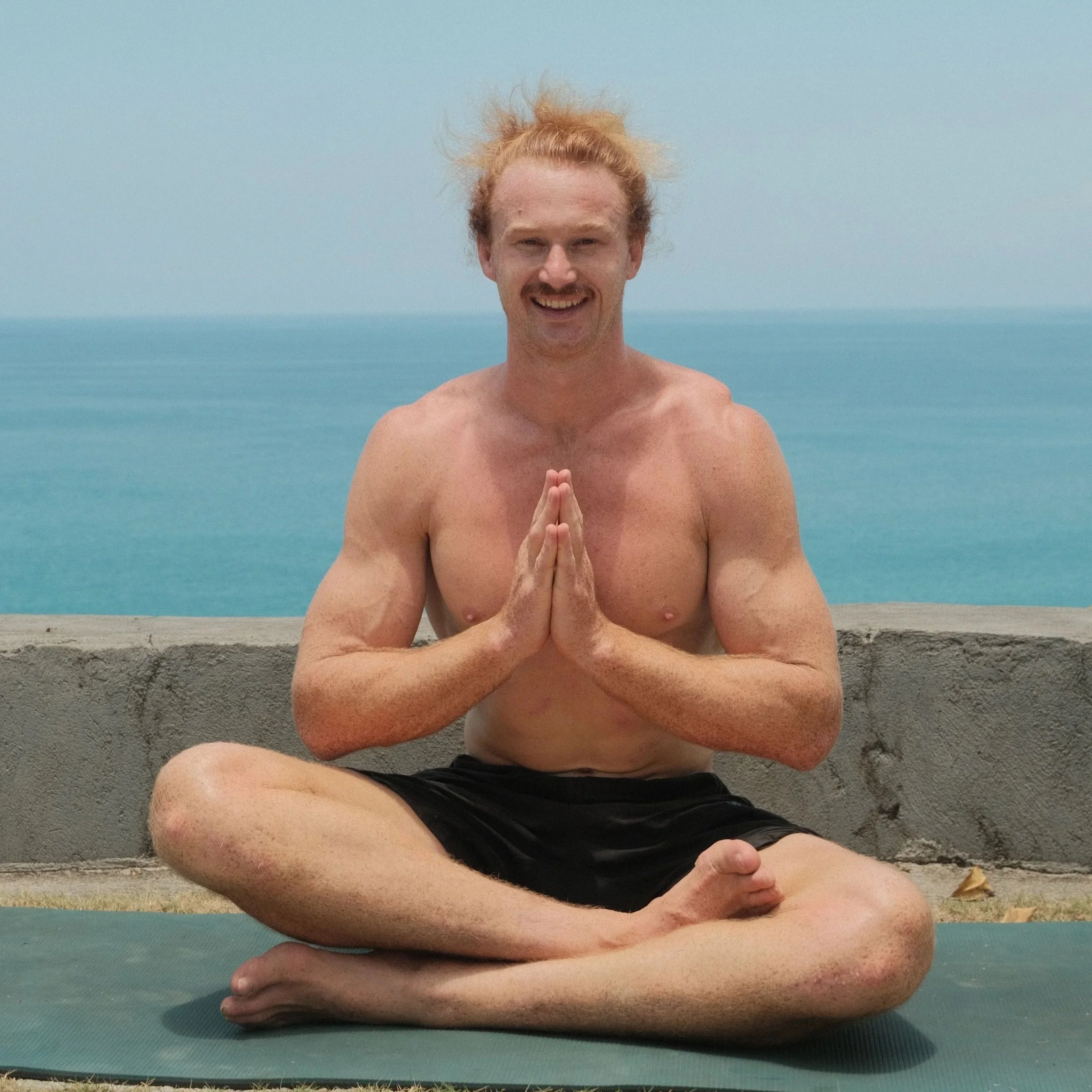 Tom Robinson, Co-Founder of Yutori Sauna, practising yoga outdoors, sitting cross-legged on a yoga mat.