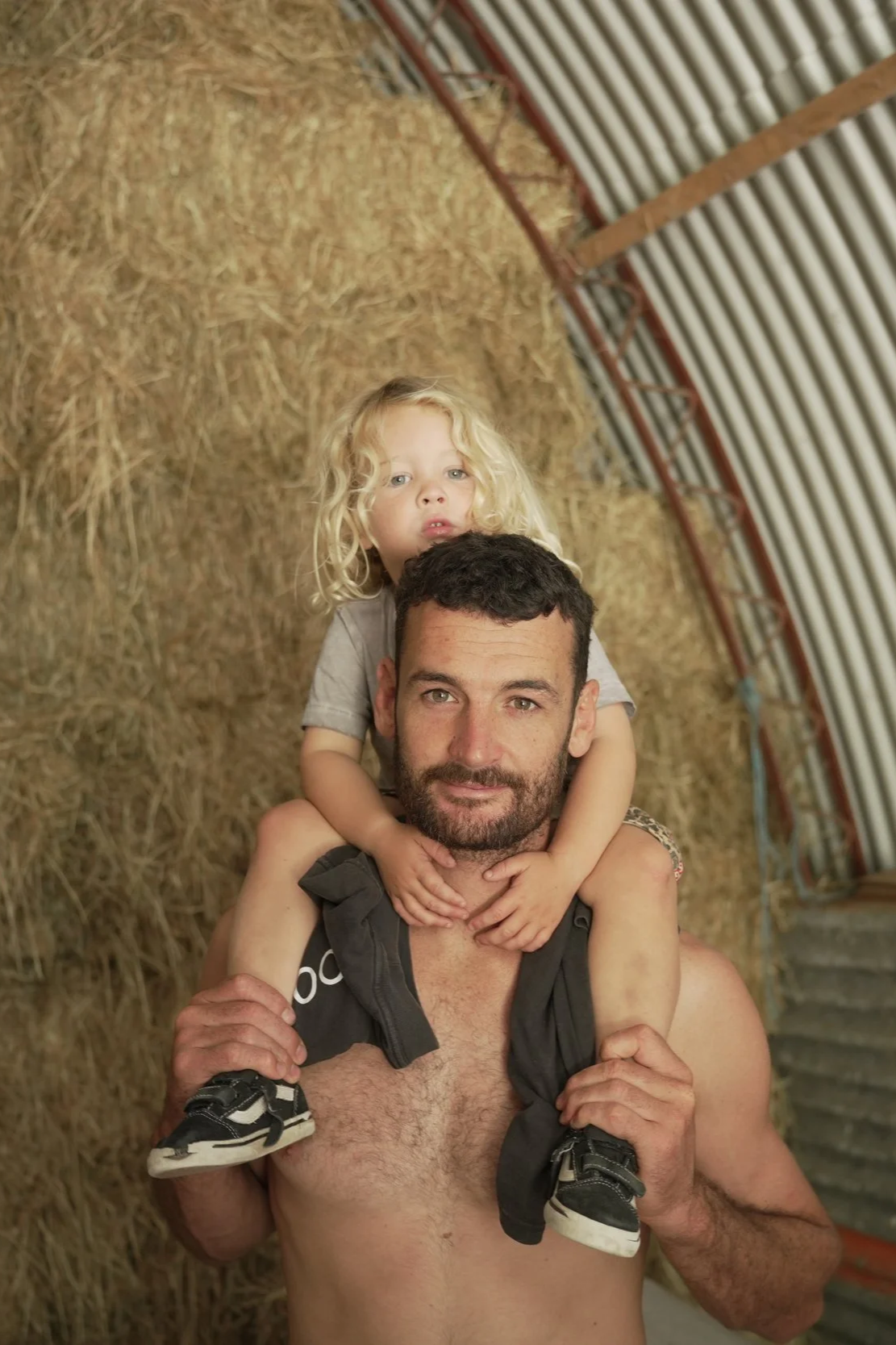 Louie Smith, Co-Founder of Yutori Sauna, with his son on his shoulders inside a barn with hay walls.