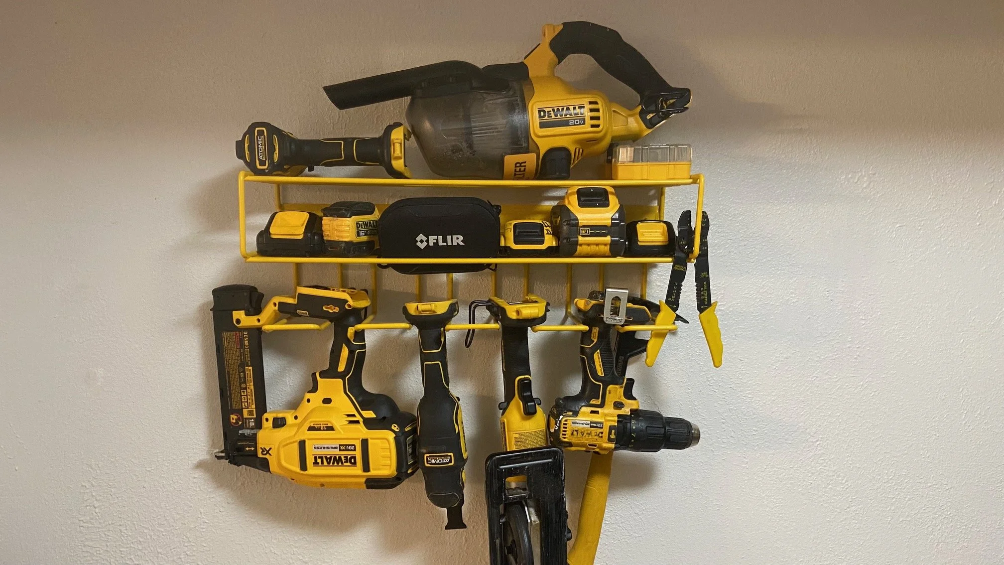 Yellow and black power tools, including drills, saw, and impact driver, arranged on yellow wall-mounted racks.