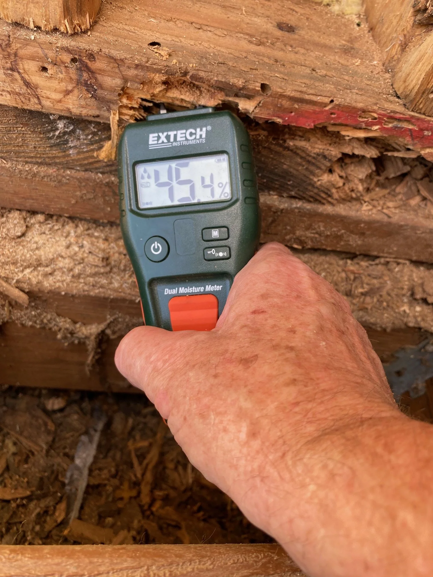 A hand holding a moisture meter in contact with a wooden surface, displaying a reading of 45.4%.