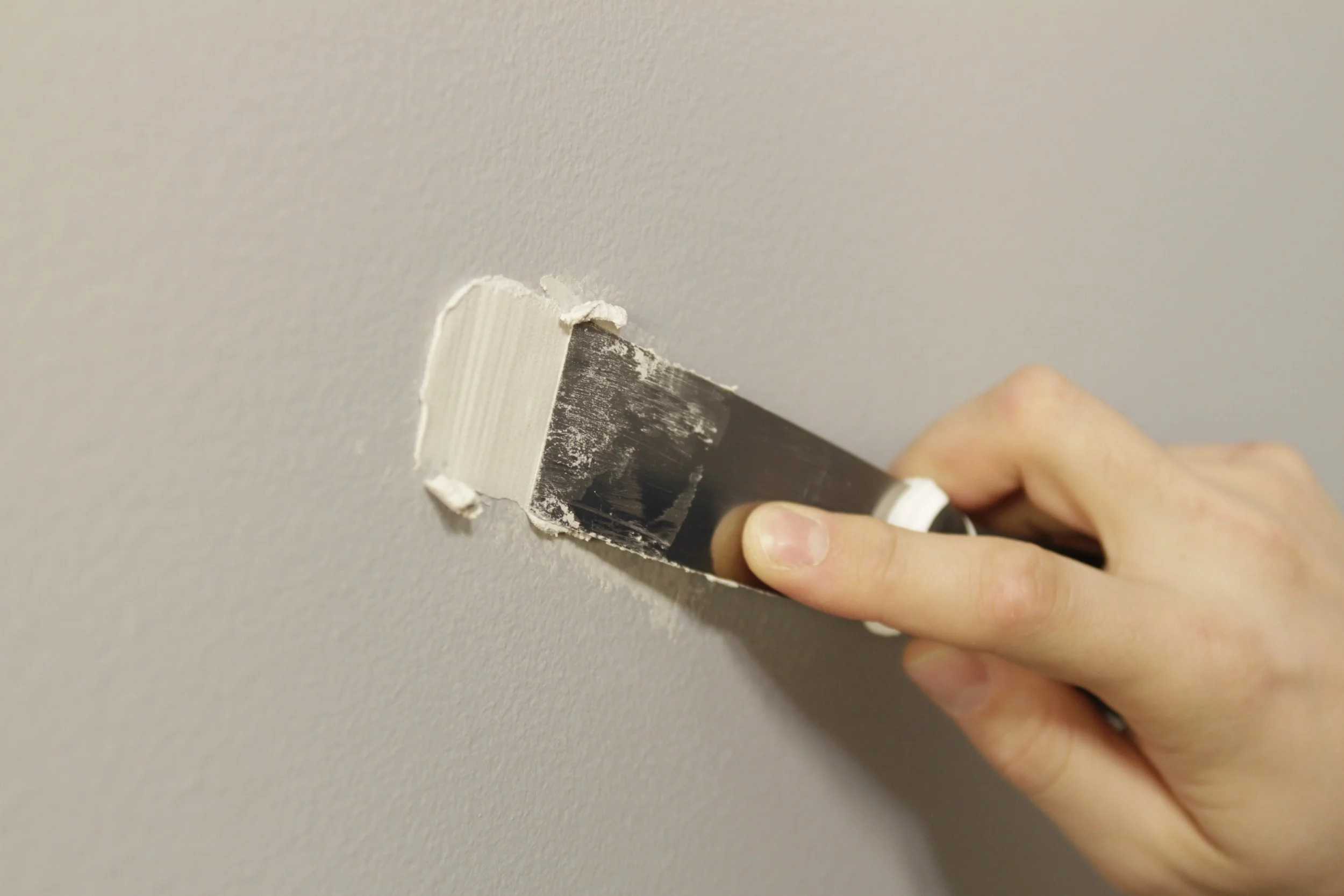 A person smoothing joint compound on a wall with a putty knife.