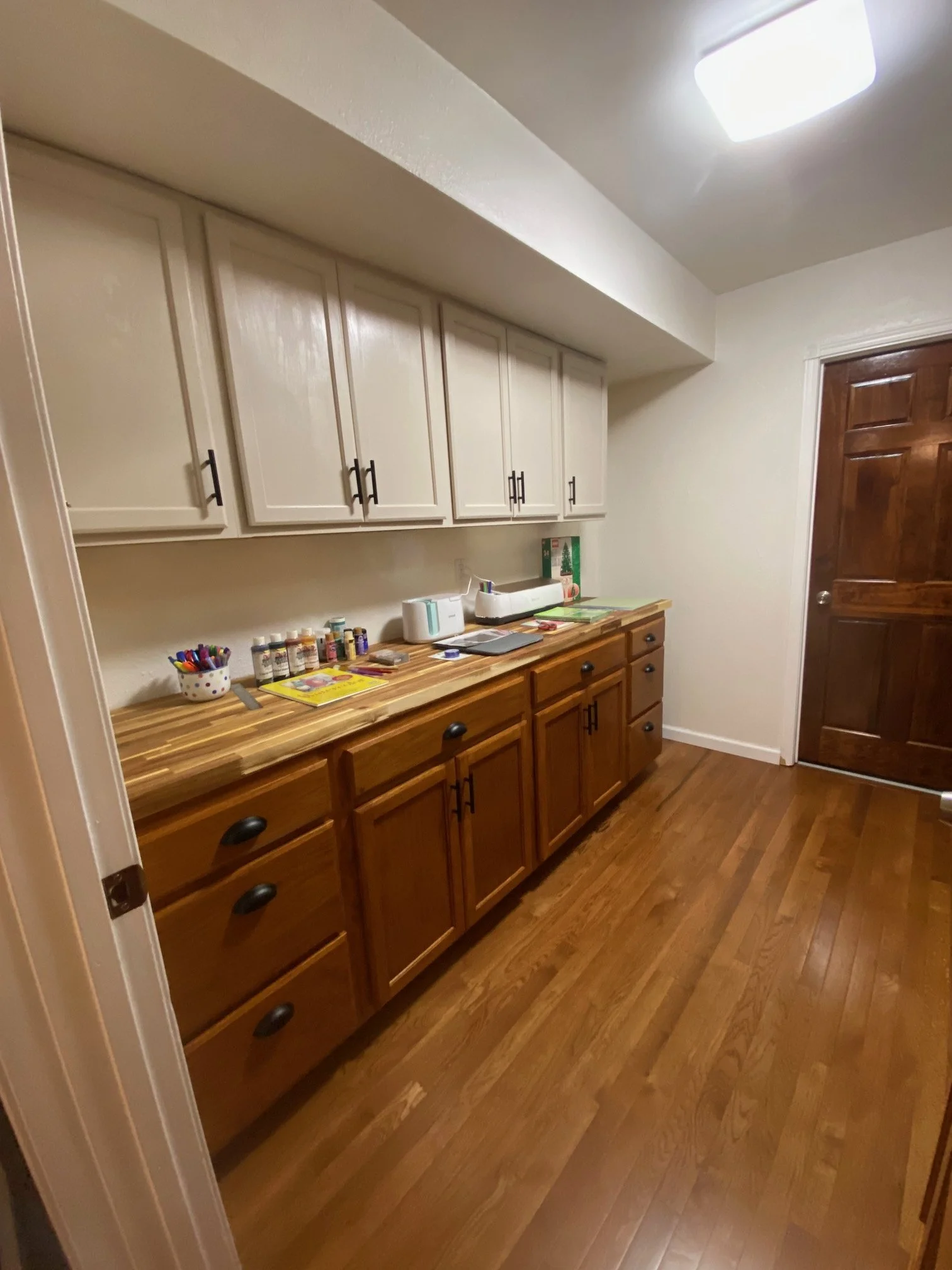 A room off the kitchen with wooden floors, white upper cabinets, and brown lower cabinets, creating a hobby room with storage.