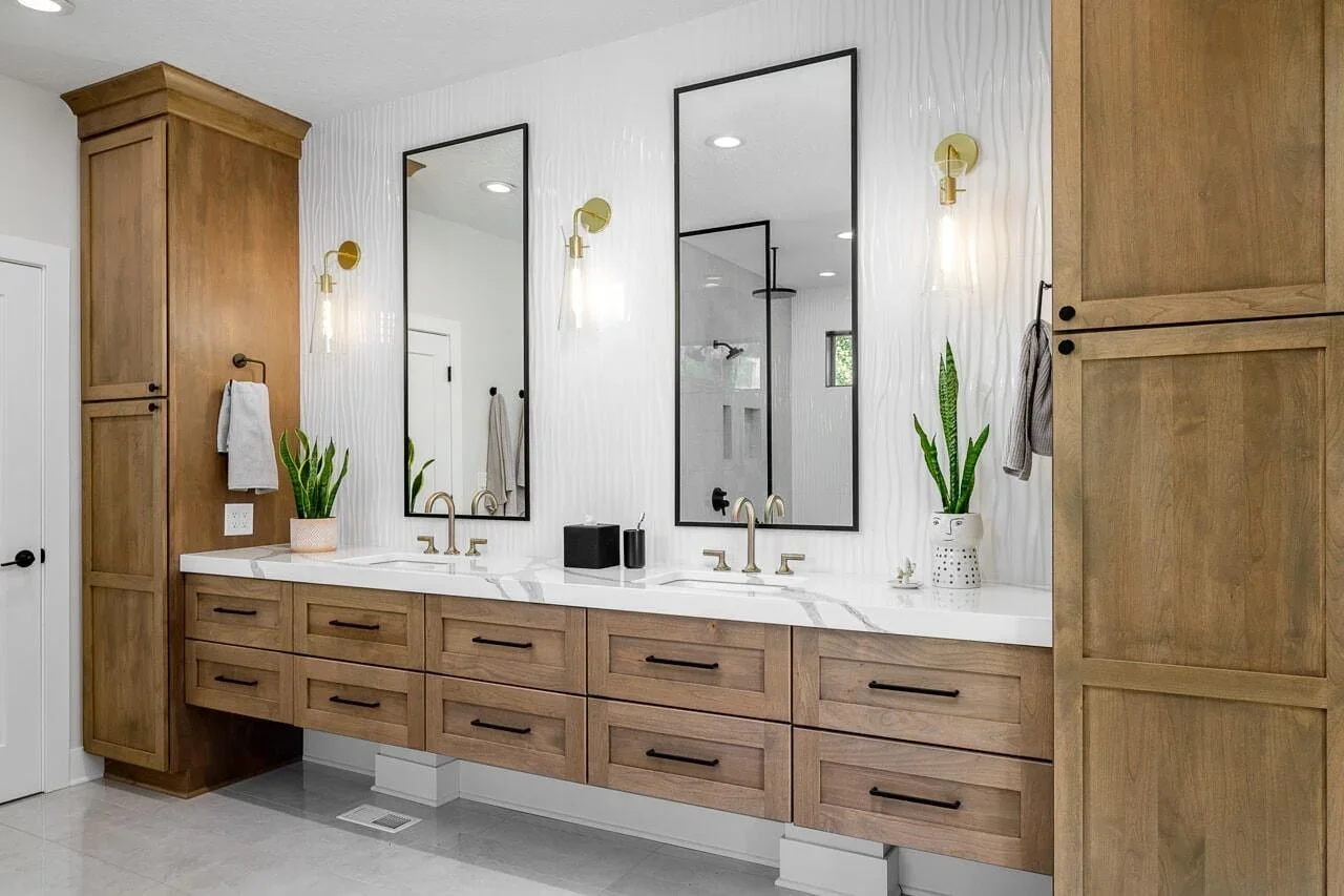Double vanity bathroom with wooden cabinetry, white marble countertop, two large mirrors, gold fixtures, and potted plants, in a modern design.