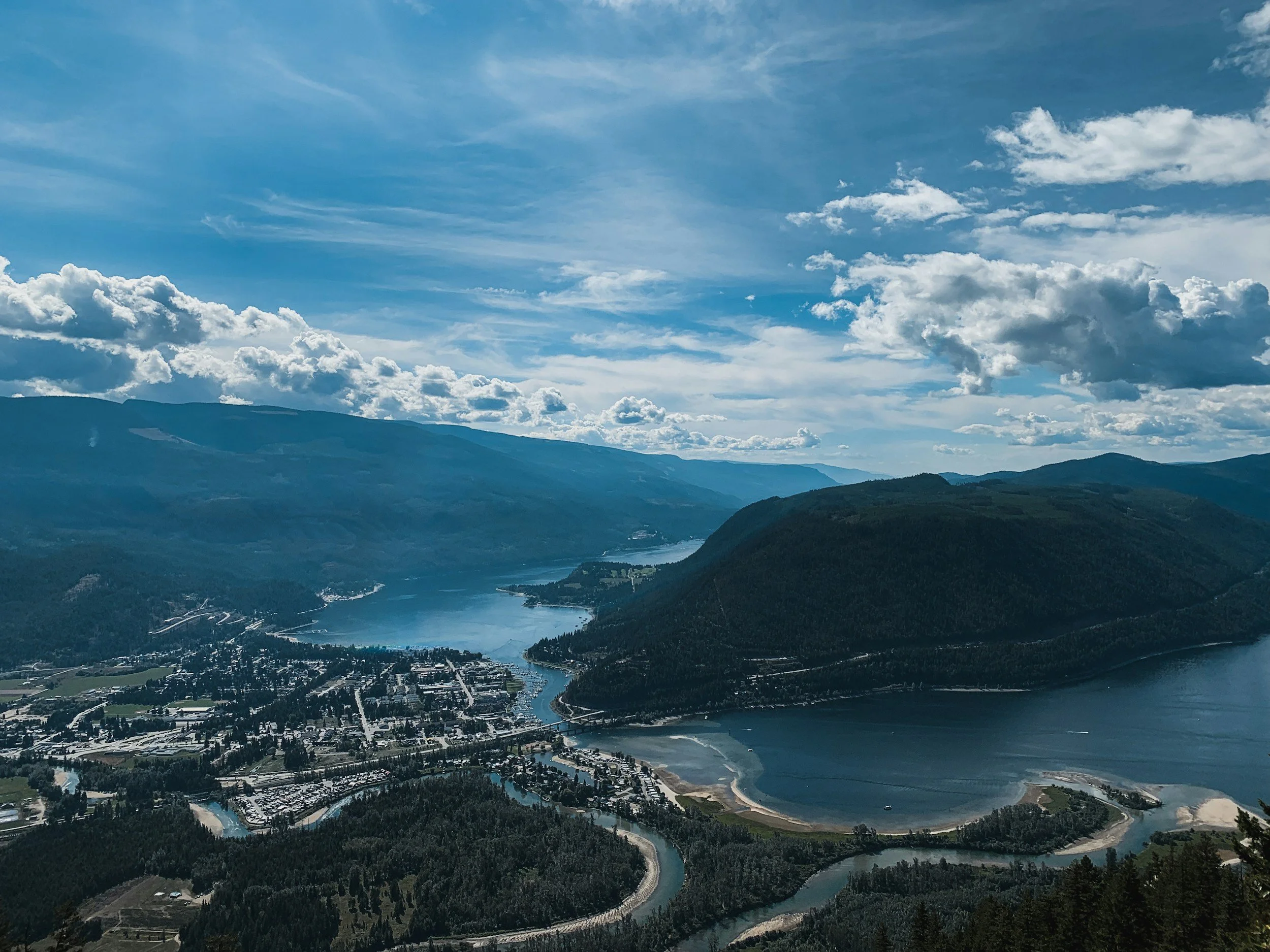 Aerial view of a town next to a river, surrounded by mountains and a partly cloudy sky.