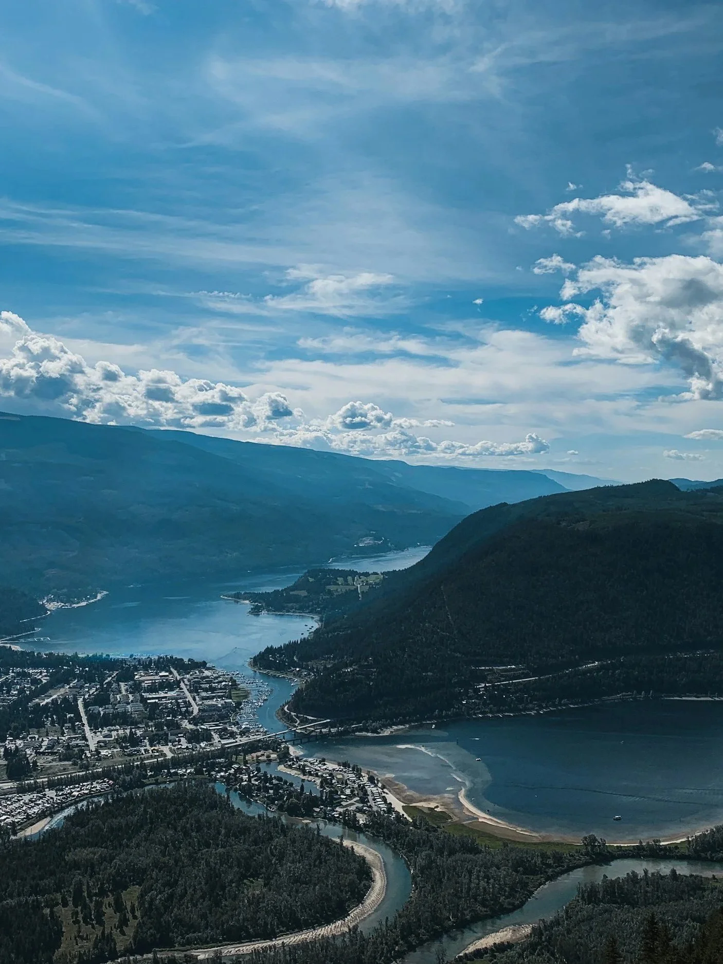 Aerial view of a river winding through a valley surrounded by green mountains under a partly cloudy sky with scattered clouds.