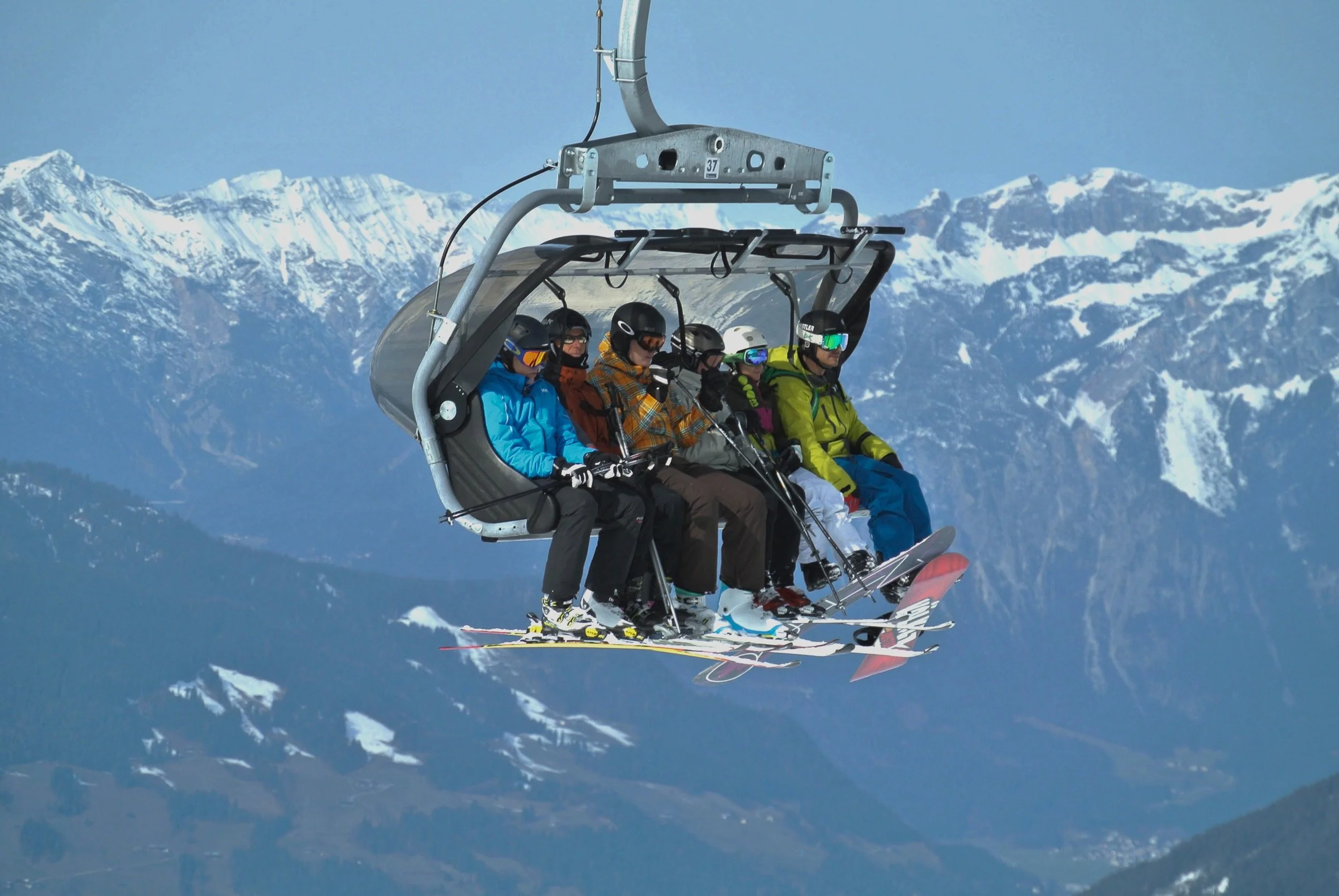 A ski lift carrying six skiers over snow-covered mountains.