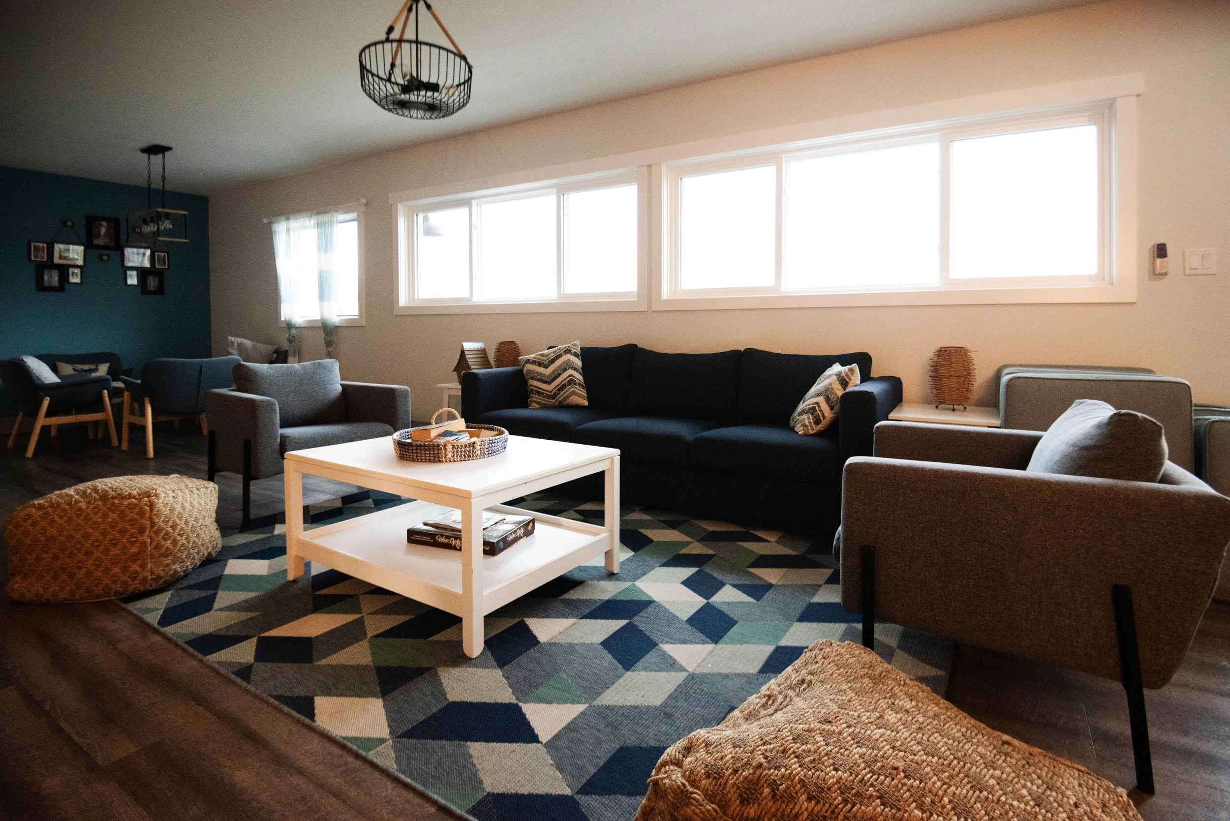 Living room with large windows, dark and light-colored sofas, patterned rug, coffee table, and wall decorations.