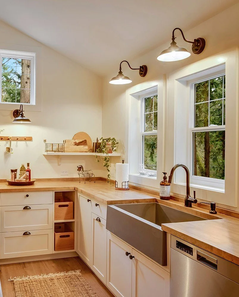 Kitchen with farmhouse style sink, wooden countertop, white cabinets, two windows, and wall-mounted light fixtures.