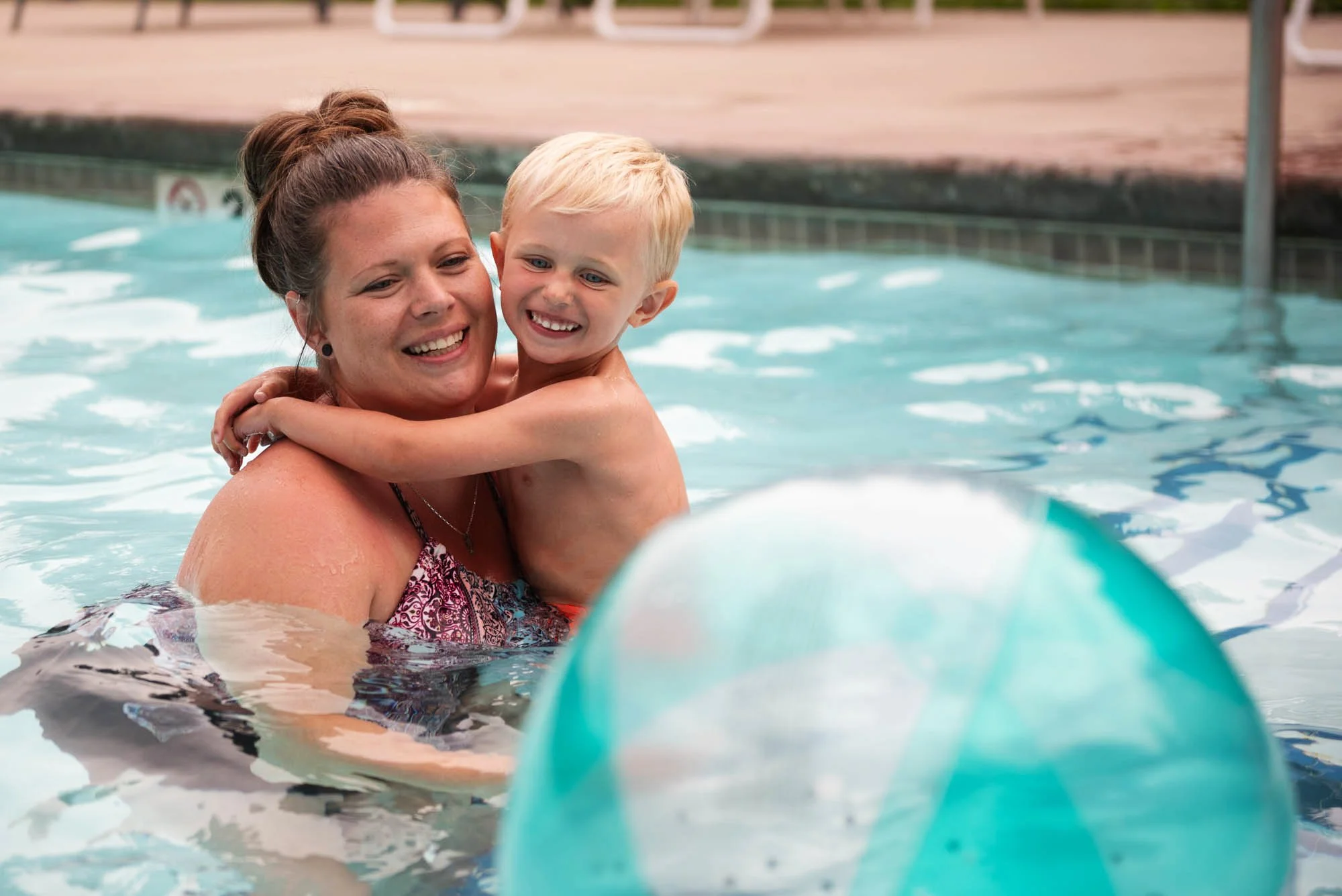 A woman and a young boy smiling and hugging in a swimming pool.