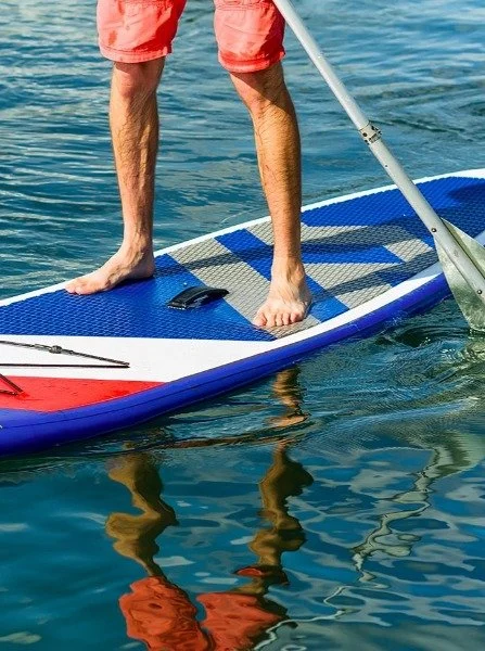 Person standing barefoot on paddleboard, using a paddle on the water, wearing red shorts.